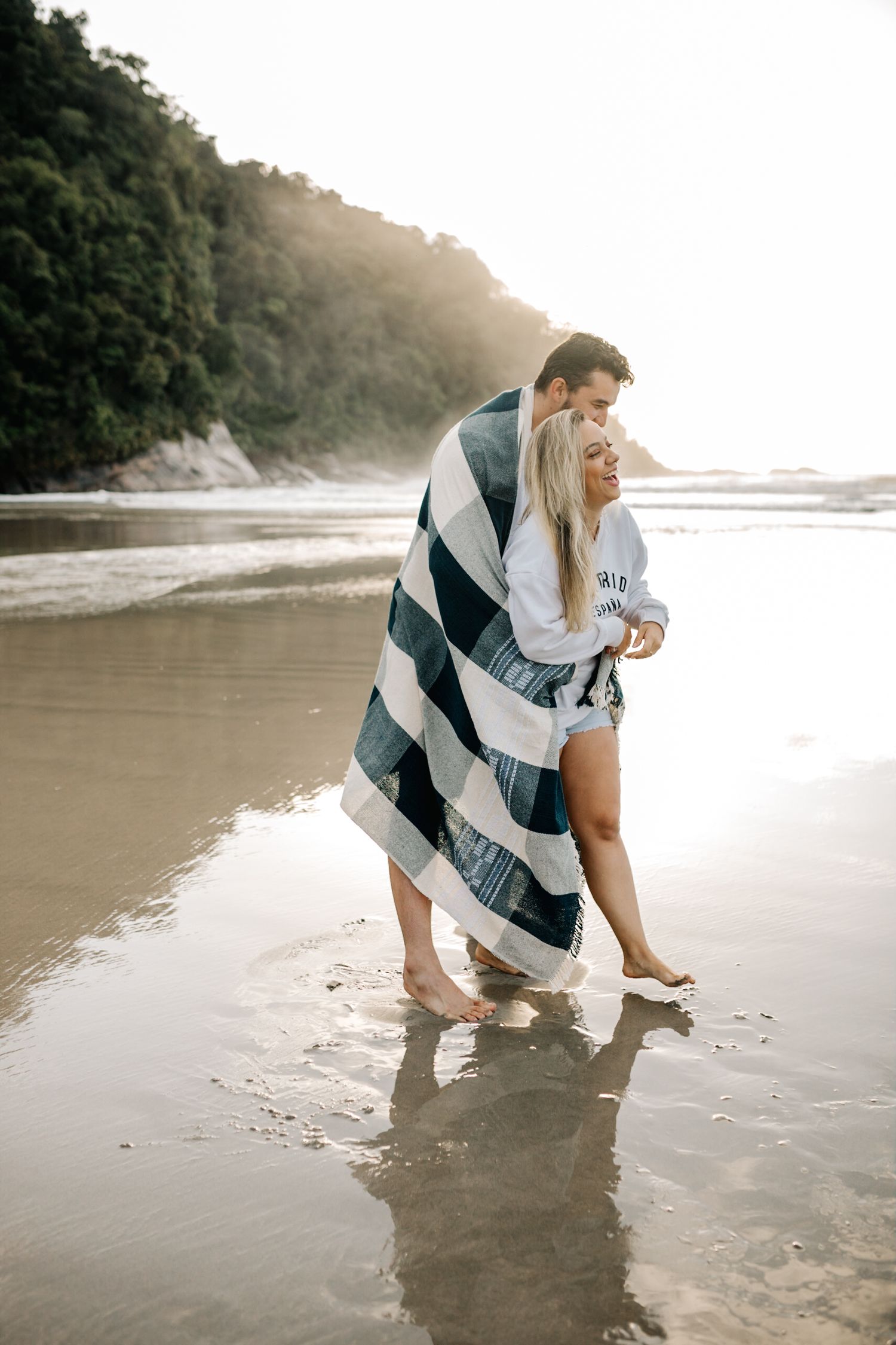 Two people playfully explore the wet sand at the water's edge during golden hour.