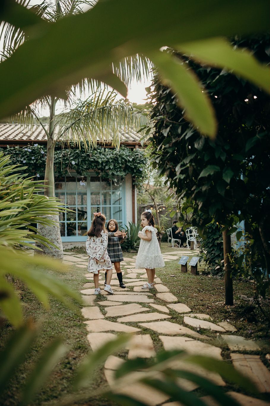 Stone pathway through garden landscape with palm fronds in foreground.