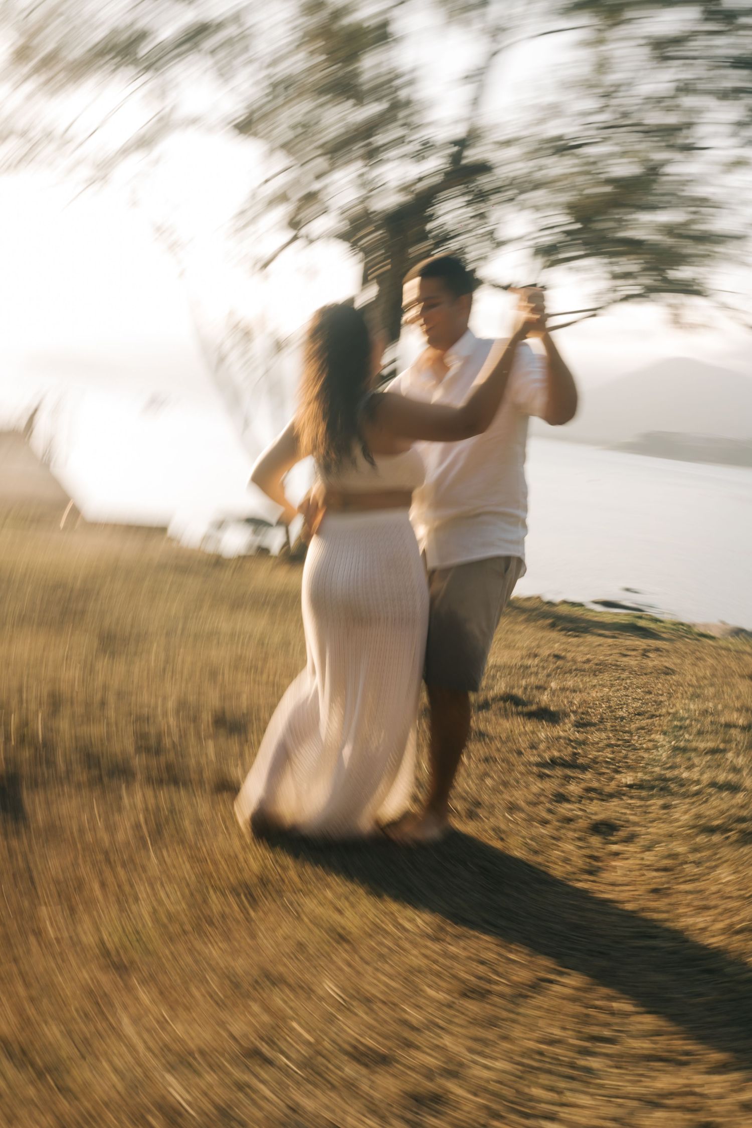 A couple dancing joyfully on a hillside during sunset with motion blur effects.