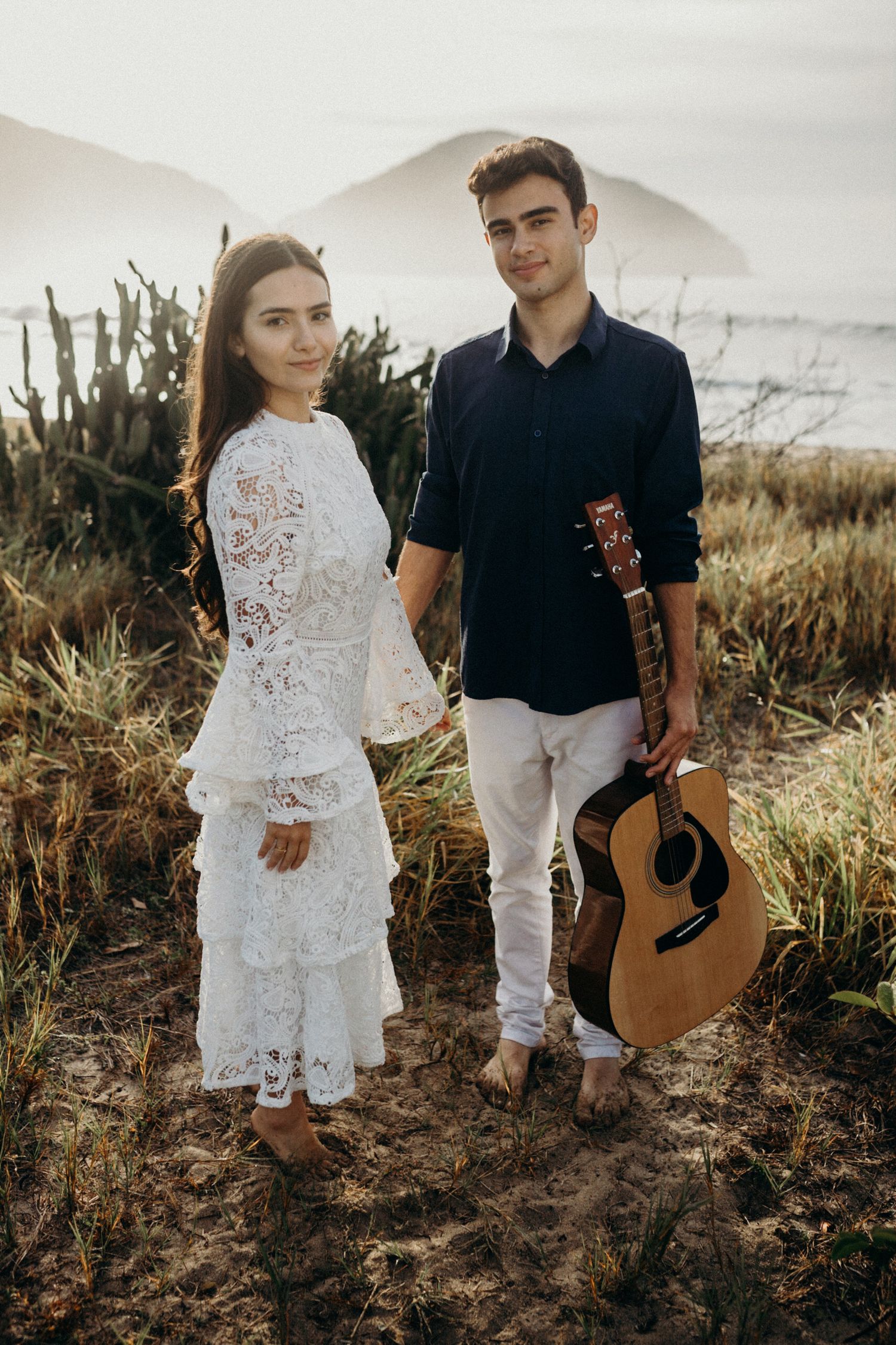 An artistic full-length portrait of a couple with an acoustic guitar against natural scenery.