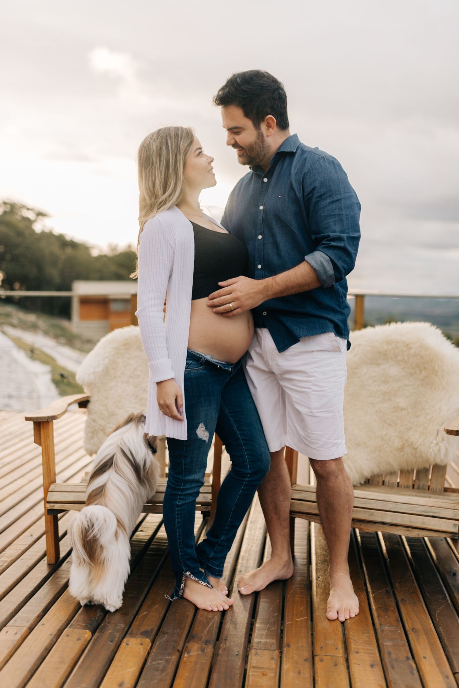 An expectant couple shares an intimate moment on a wooden deck with scenic views.
