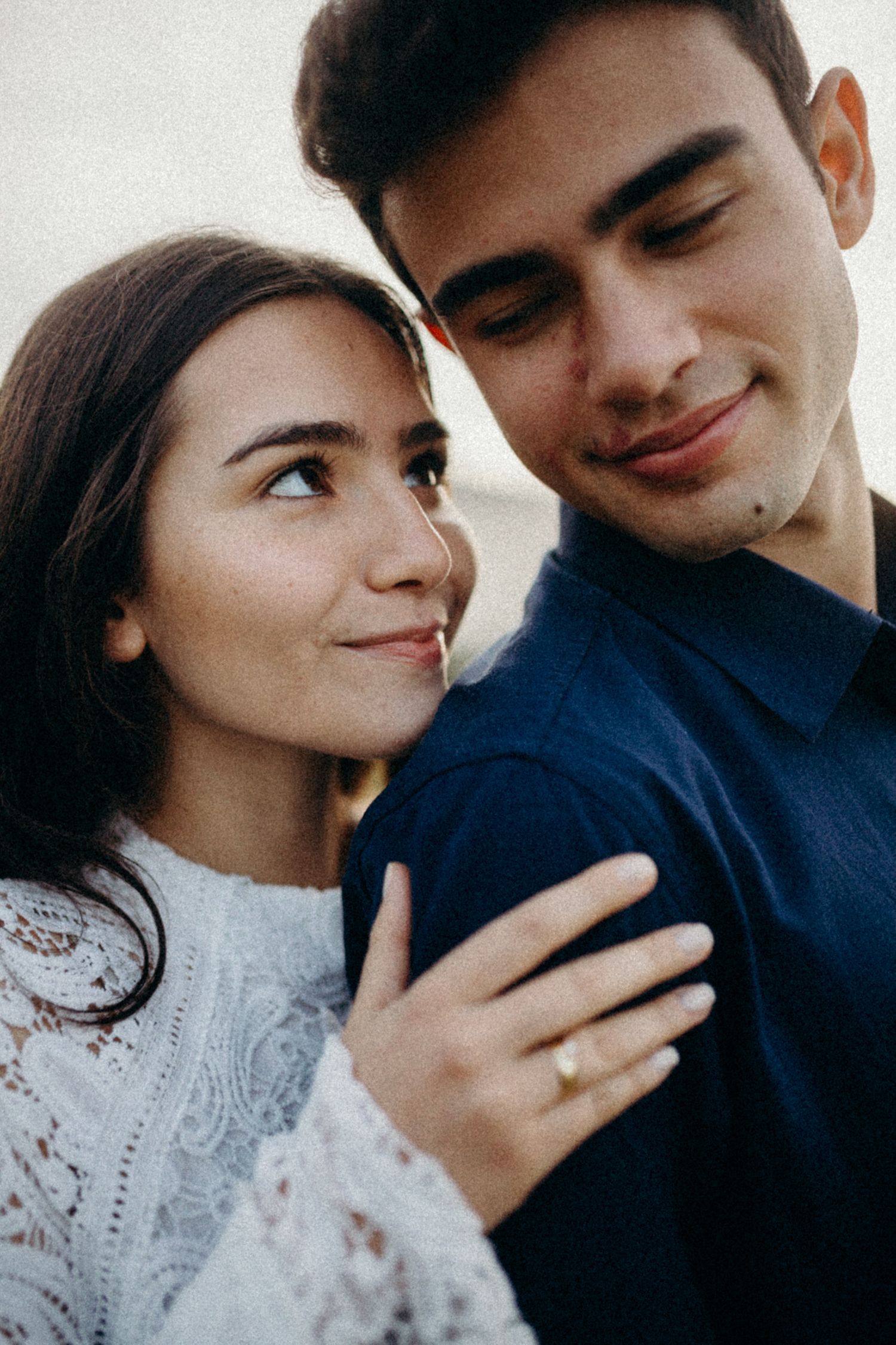 A tender romantic portrait of a couple in a navy shirt and white lace dress sharing an intimate moment.