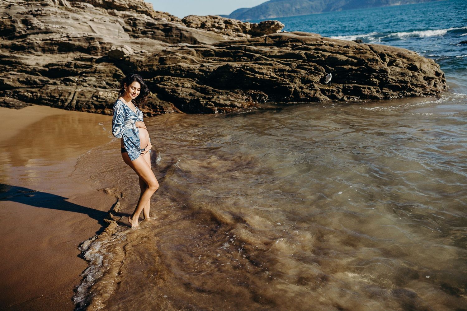 A beachside maternity portrait with coastal rocks and waves in Hawaii.