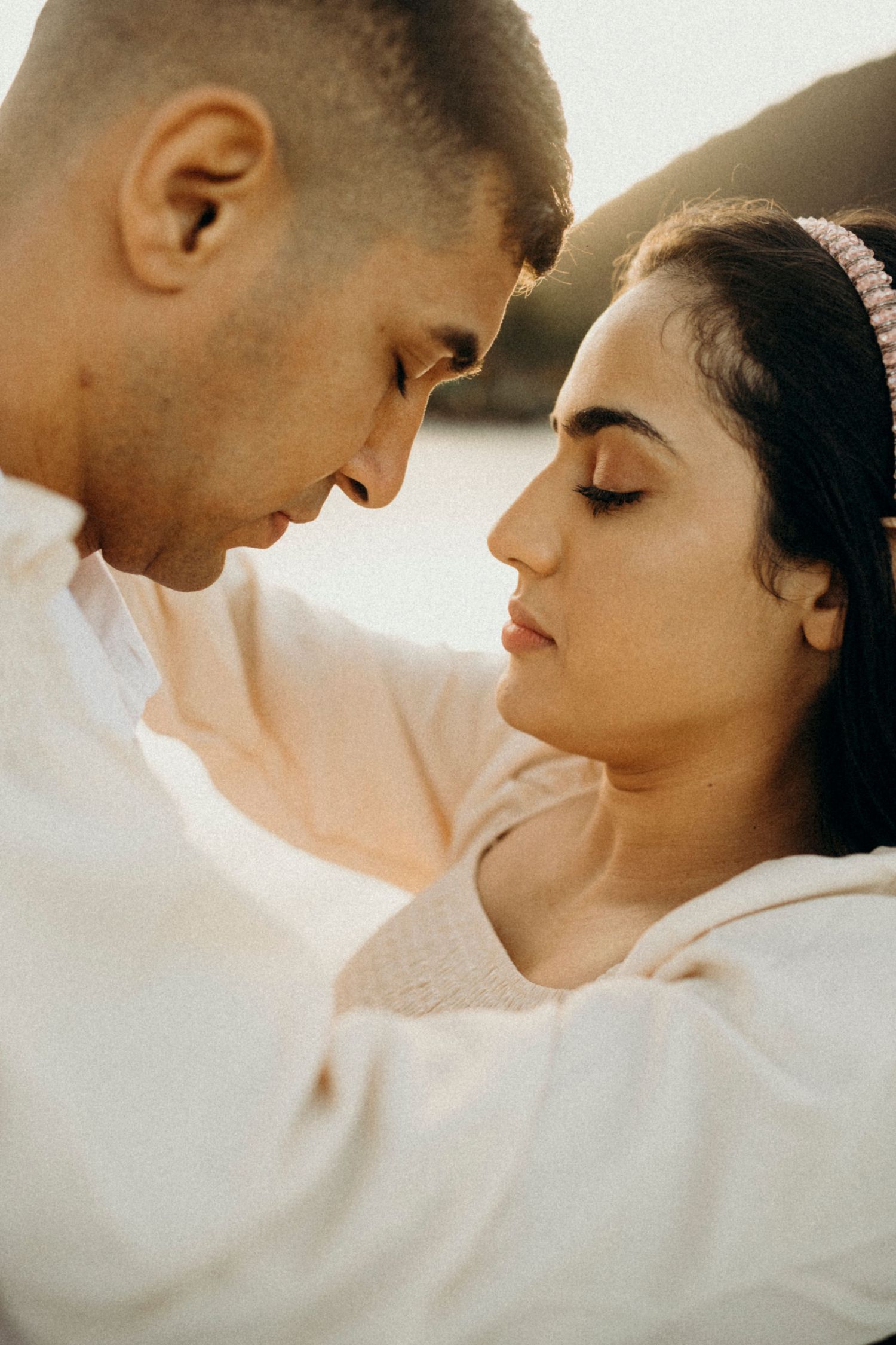A tender close-up portrait of a couple in white clothing against a bright background.