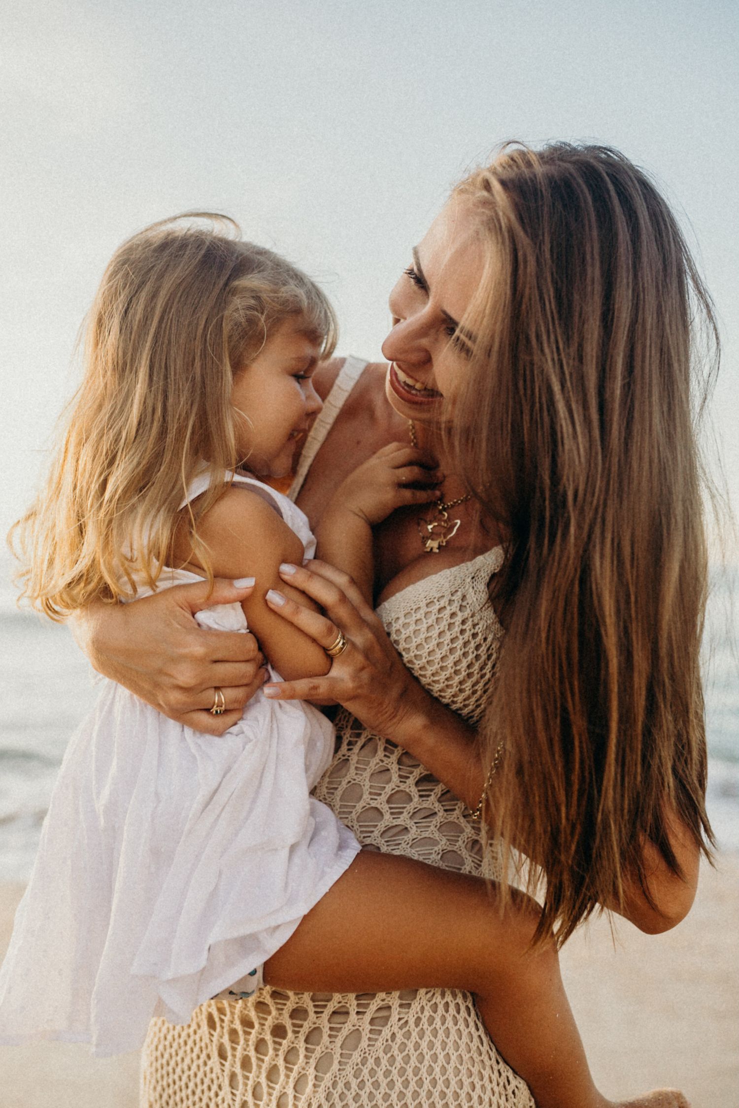 A playful beach moment between parent and child in white clothing with golden sunlight.