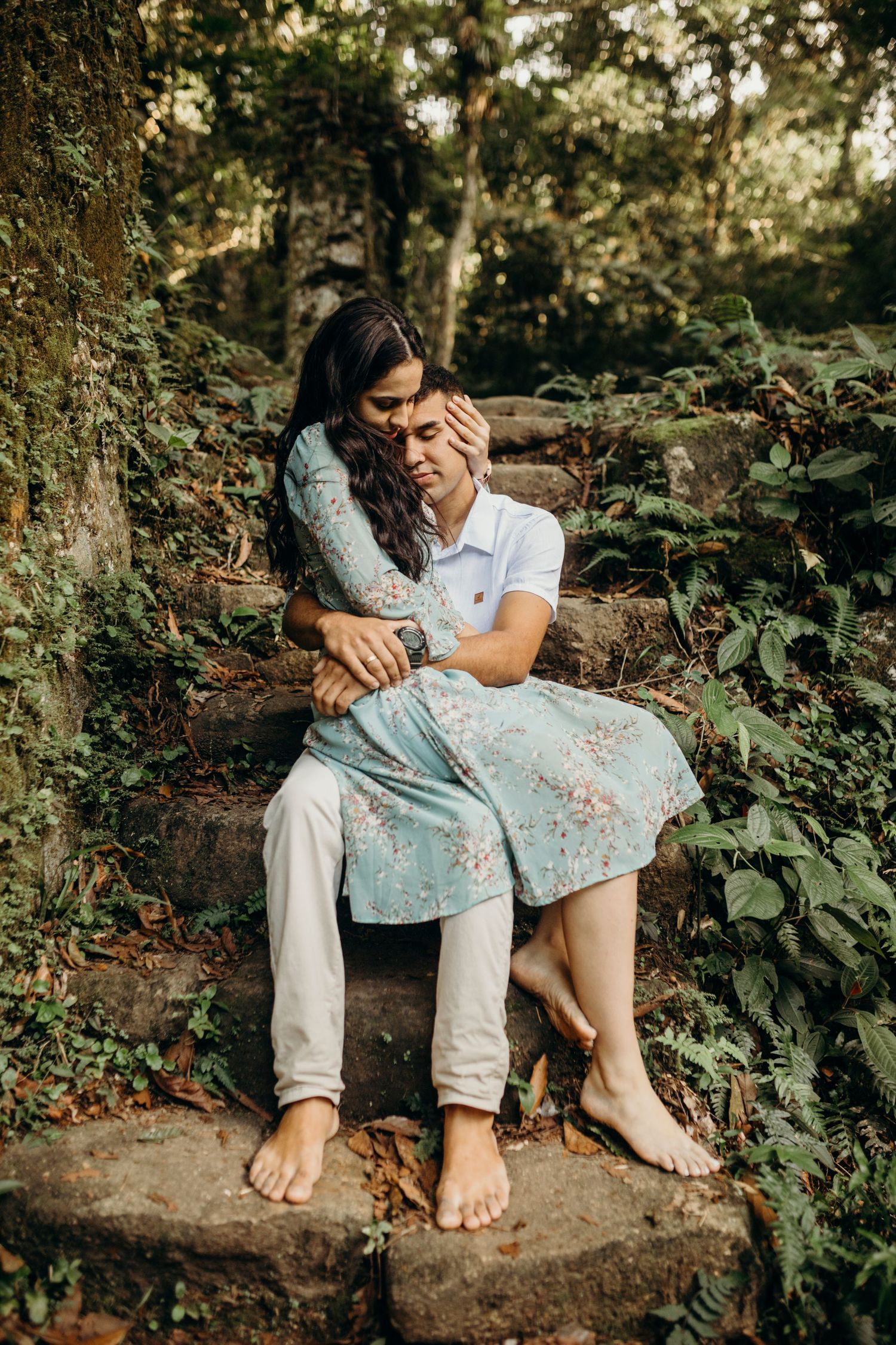 Couple in coordinated white and blue outfits sharing a romantic moment on stone steps in nature.