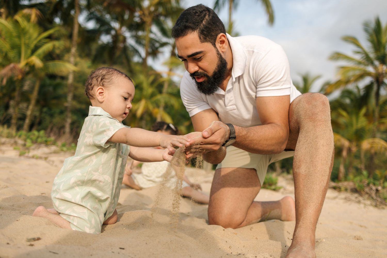 Parent and child playing together with sand toys on a tropical beach with palm trees in the background.