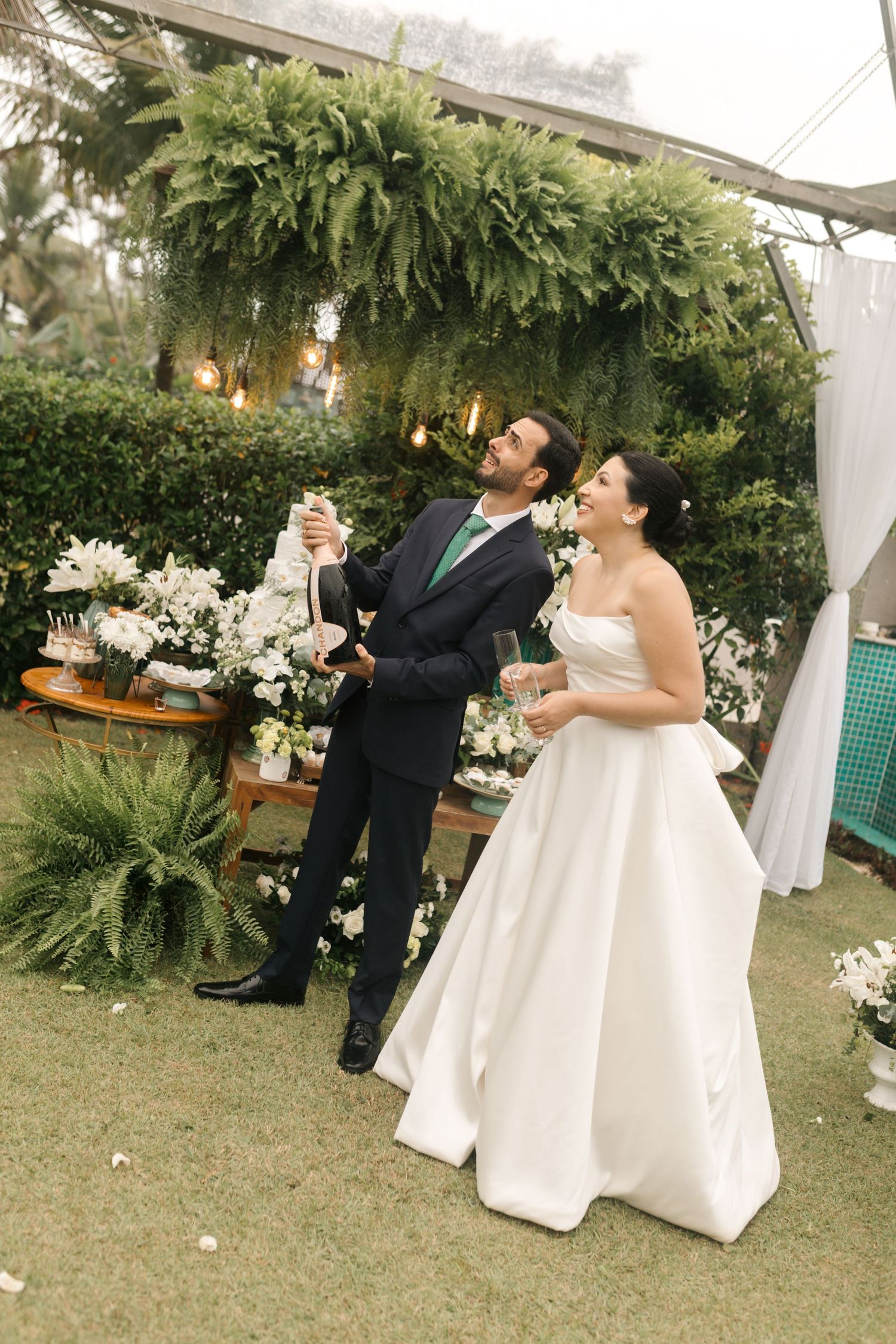 Wedding celebration under a lush green canopy with floral decorations.