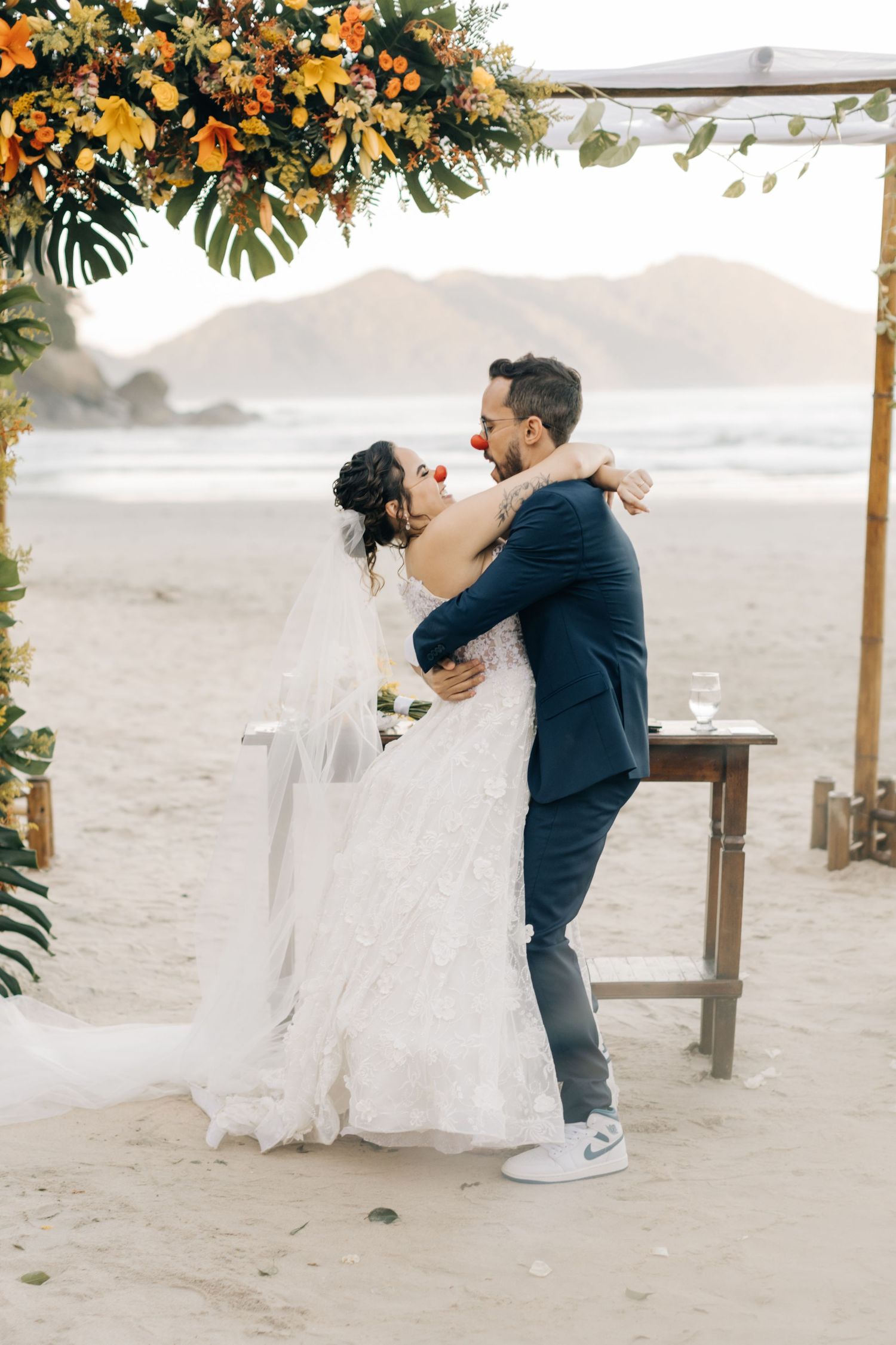 Sunset beach wedding celebration with couple dancing beneath tropical floral arrangements.