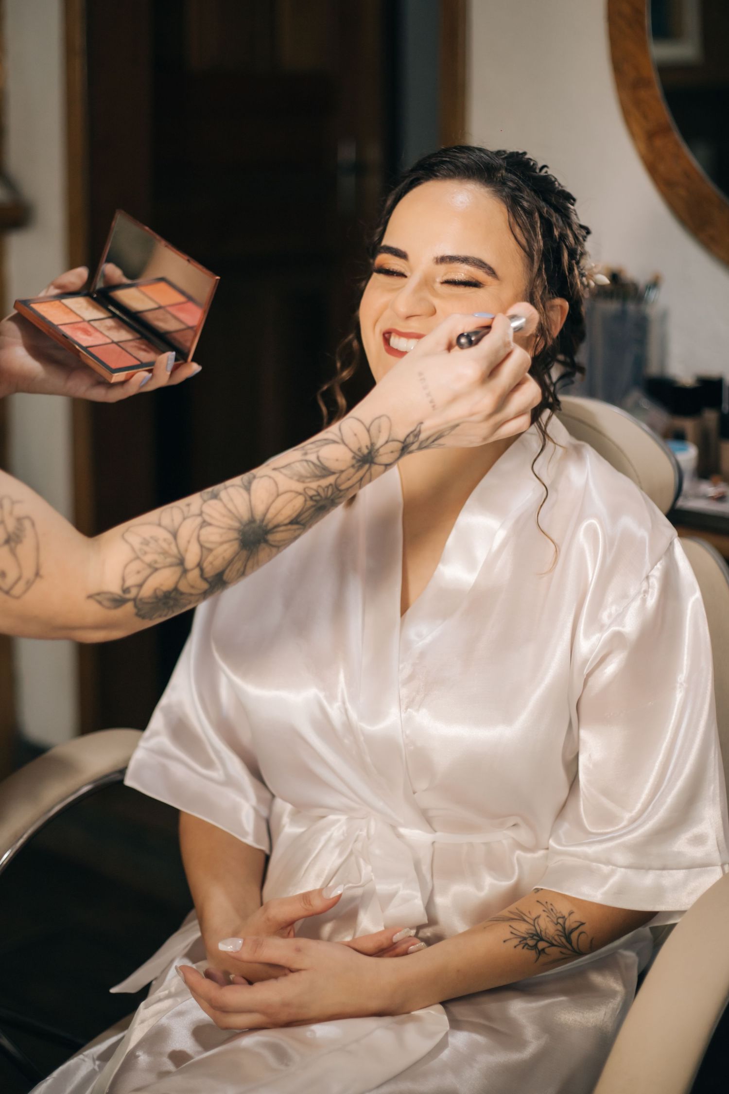 Makeup artist applying cosmetics to smiling client in white silk robe.