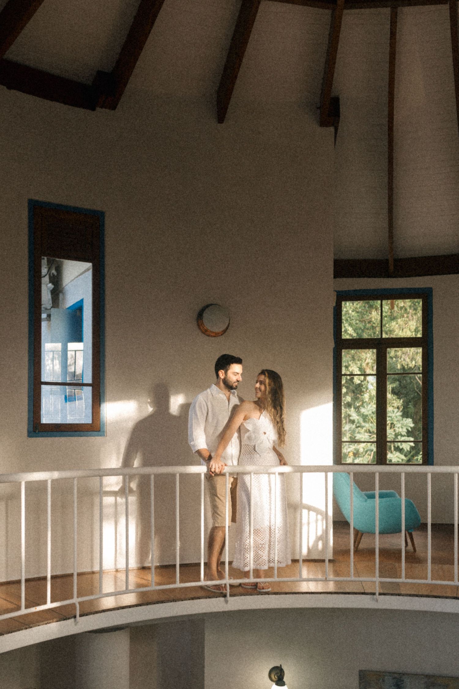 A couple shares an intimate moment on a curved balcony in a room with high vaulted ceilings.