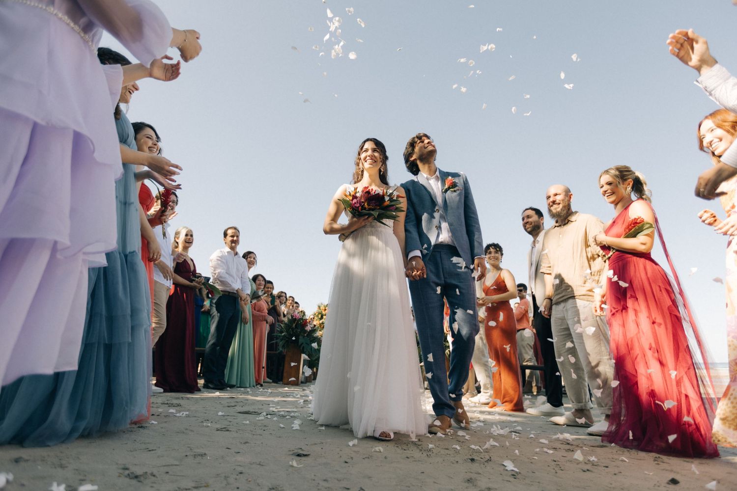 Wedding guests throw flower petals during an outdoor celebration.