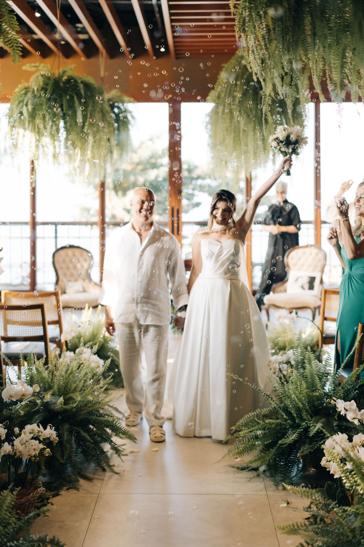 Newlyweds celebrate with guests as bubbles float through the air in a decorated venue.