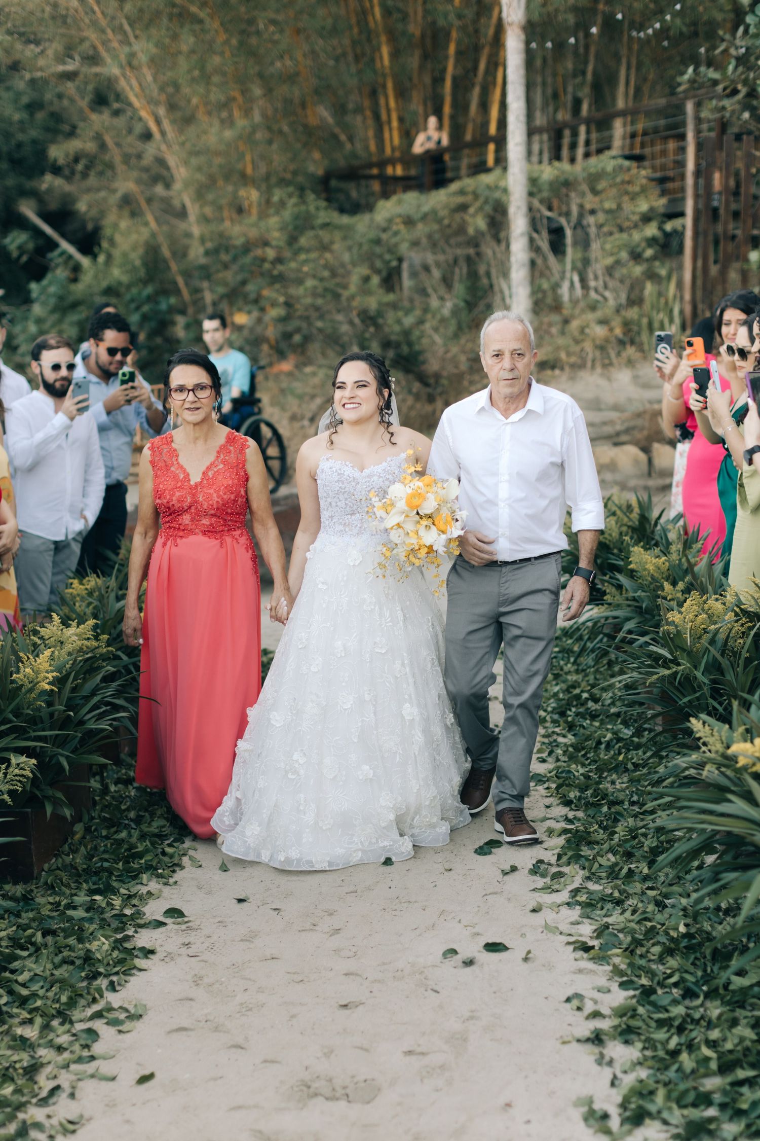 A wedding procession walks down a garden path lined with tropical plants.