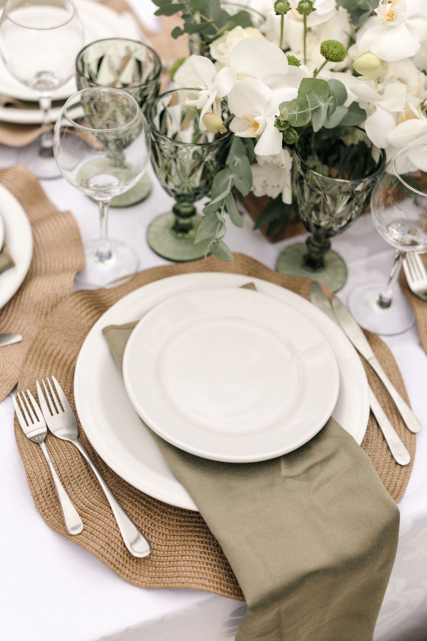 Wedding table setting with delicate white flowers, natural placemats, and sage green napkins.
