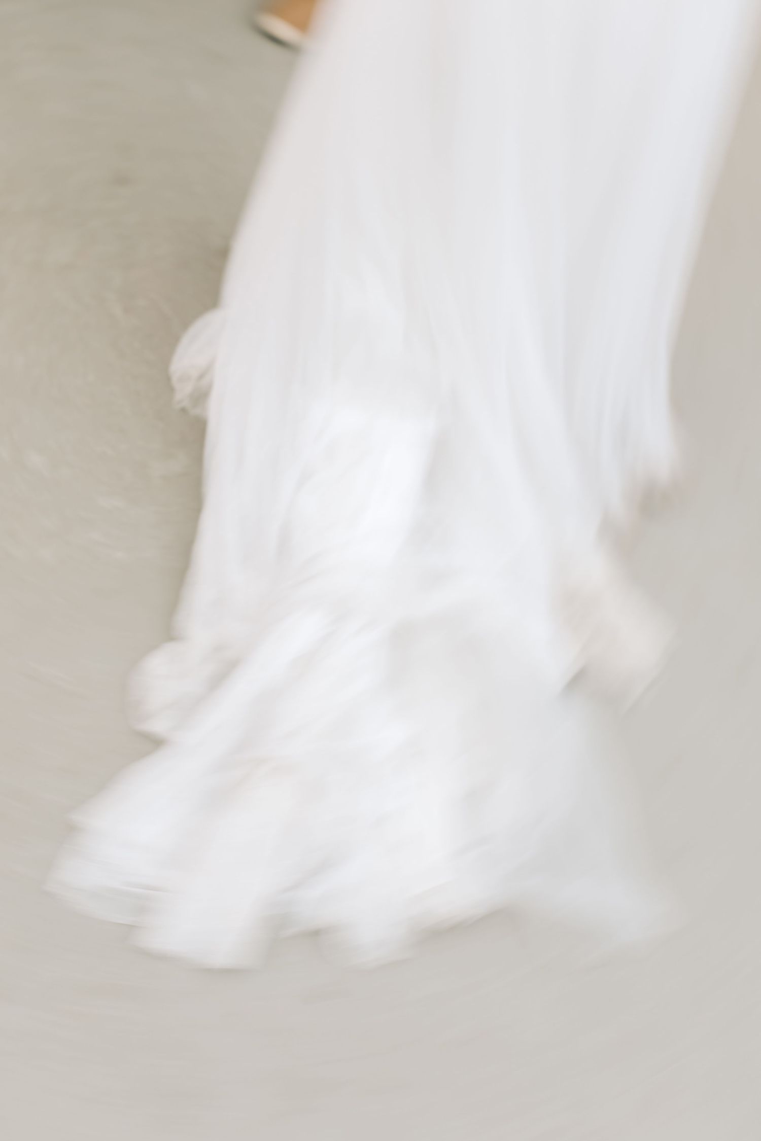Motion blur of flowing white wedding dress fabric against light floor.