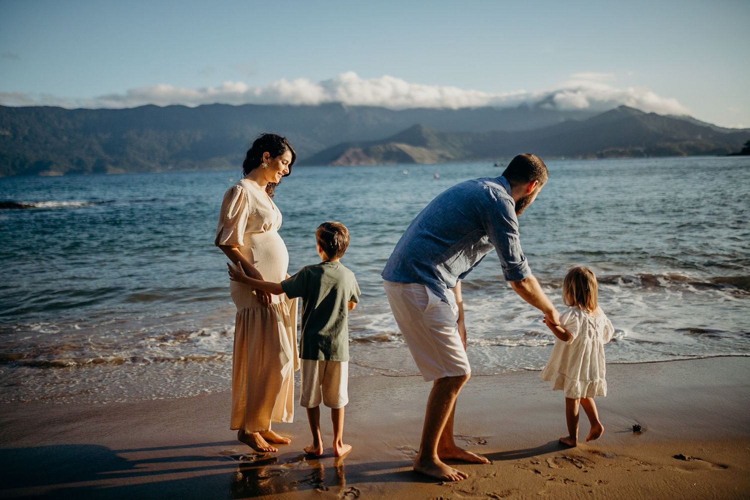 Family enjoying a playful moment together at the beach during sunset with mountains in background.