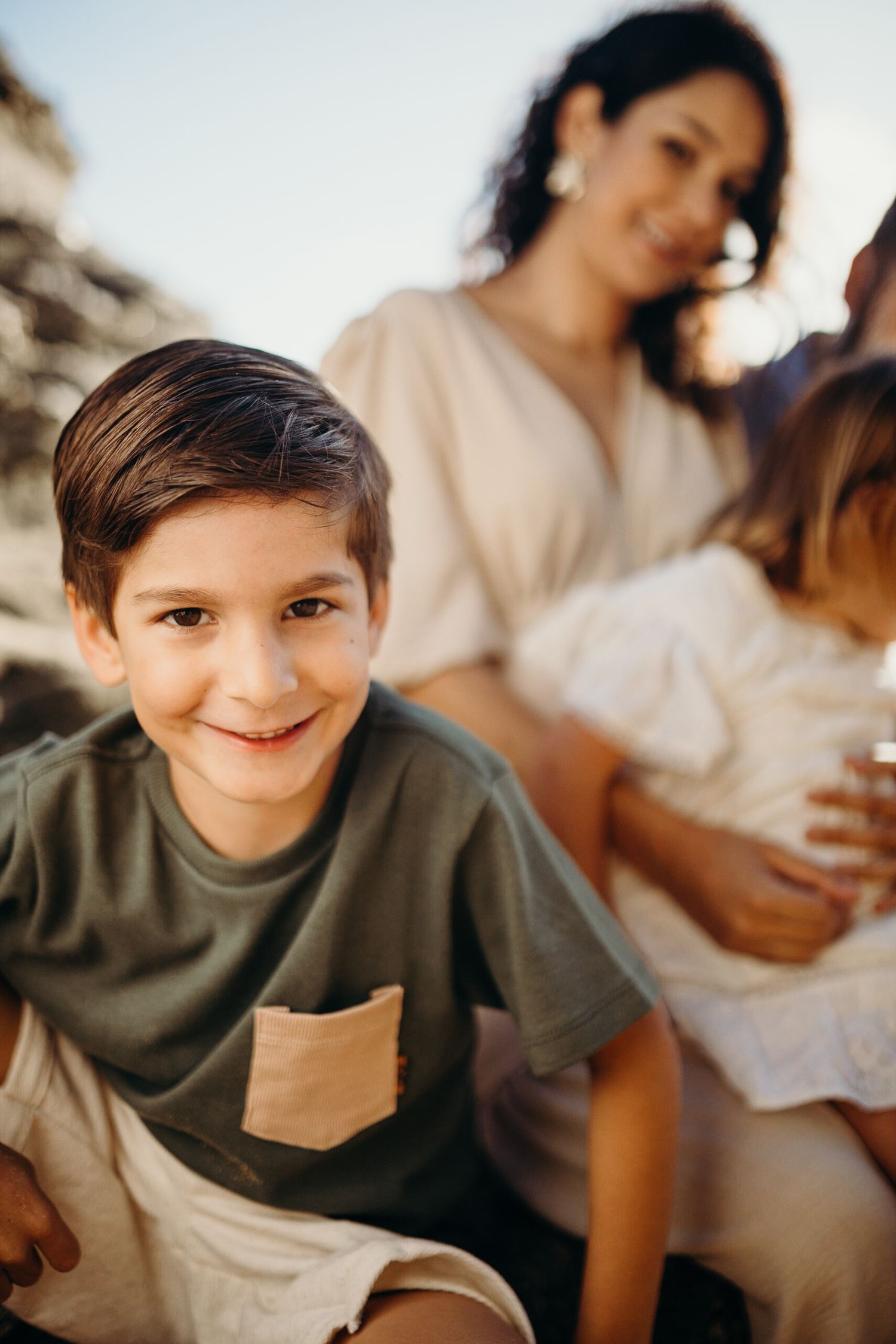 A casual family portrait session on rocky beach terrain during golden hour.