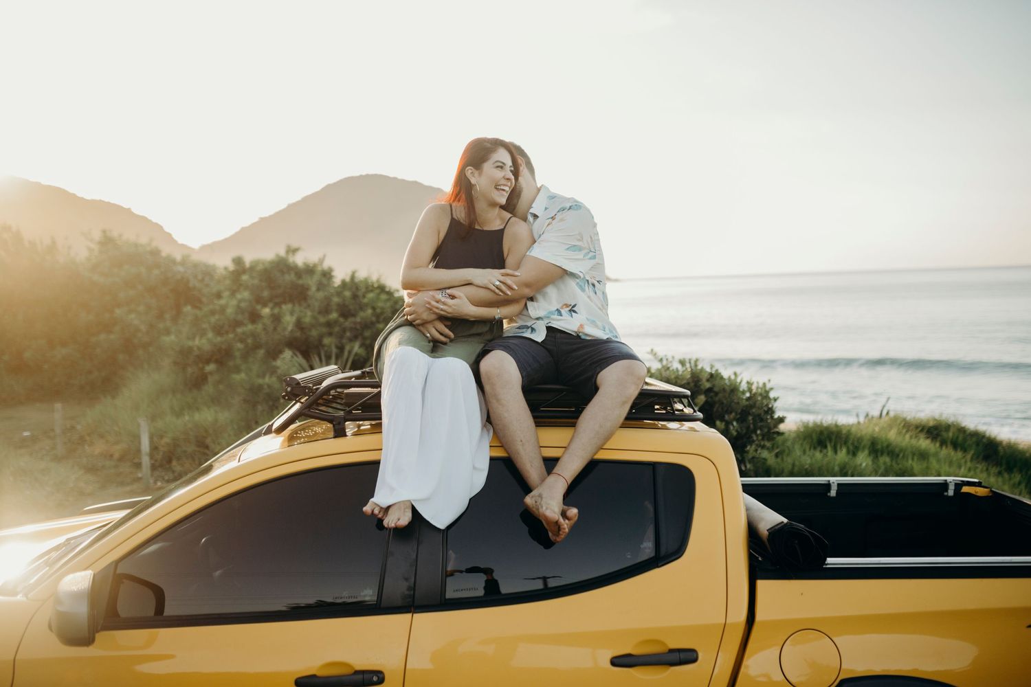 Intimate photoshoot on a yellow pickup truck with ocean and mountains in background.