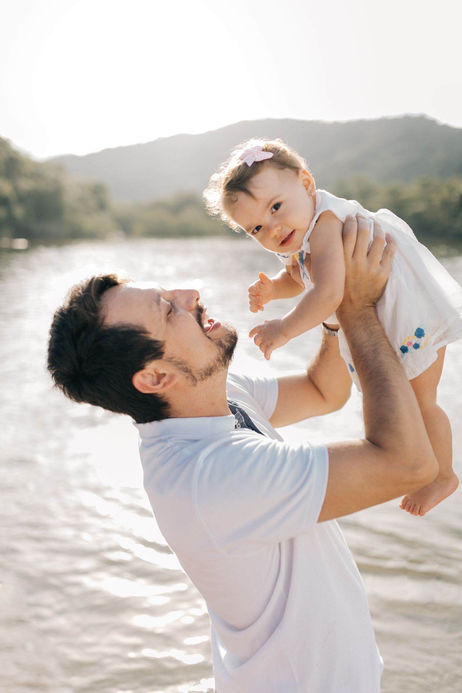 A joyful moment captured at sunset as a baby is lifted high by loving arms near a mountain lake.