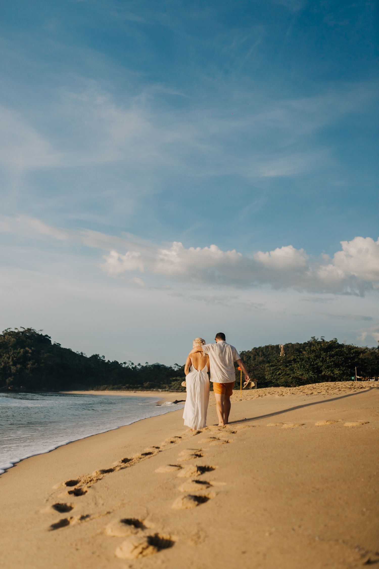 Couple walking away on empty beach with footprints trailing behind in golden sand.