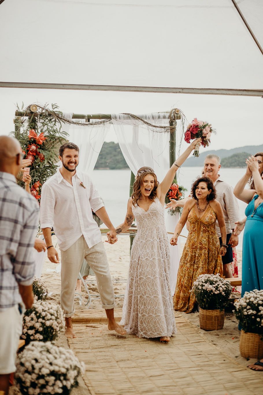 Guests in light colored attire dance joyfully at an open-air beach wedding reception.