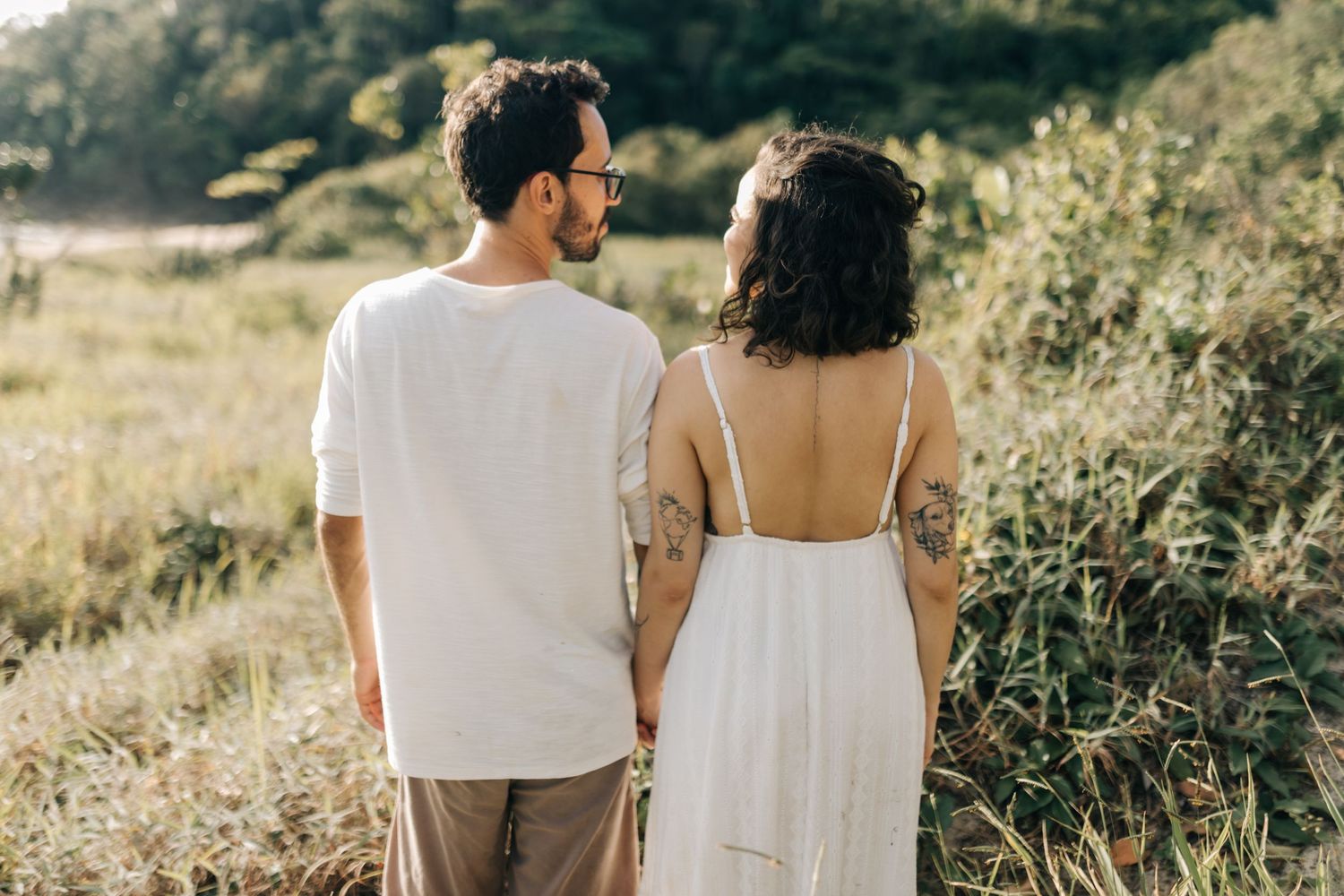 Couple in white clothing walking together on a scenic hillside trail.