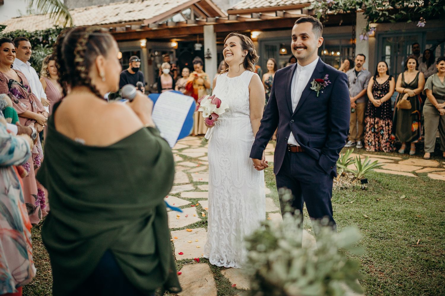 Guests observe an outdoor wedding ceremony in front of a Spanish-style building.