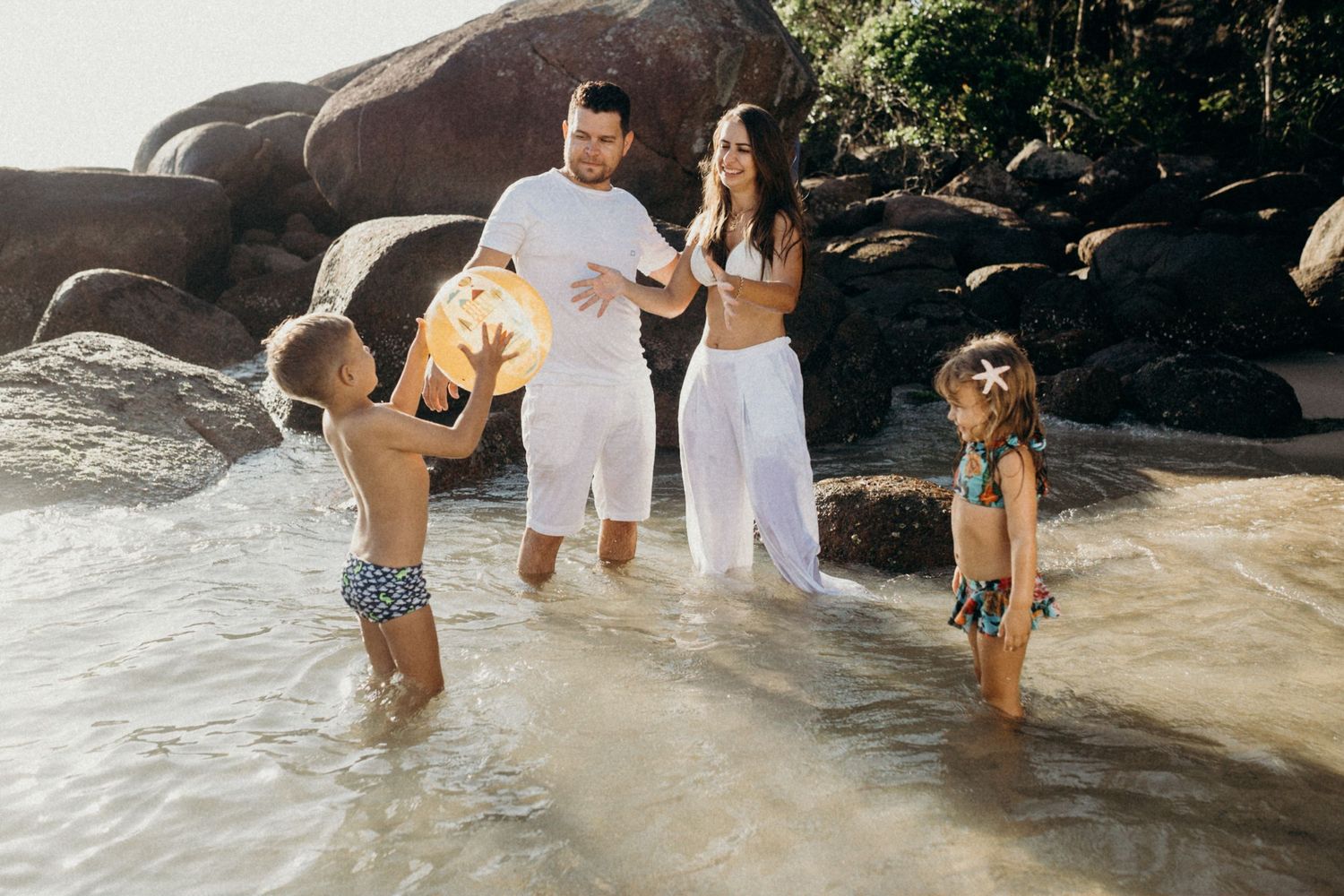 Group enjoying beach day splashing in shallow water near rocky coastline.