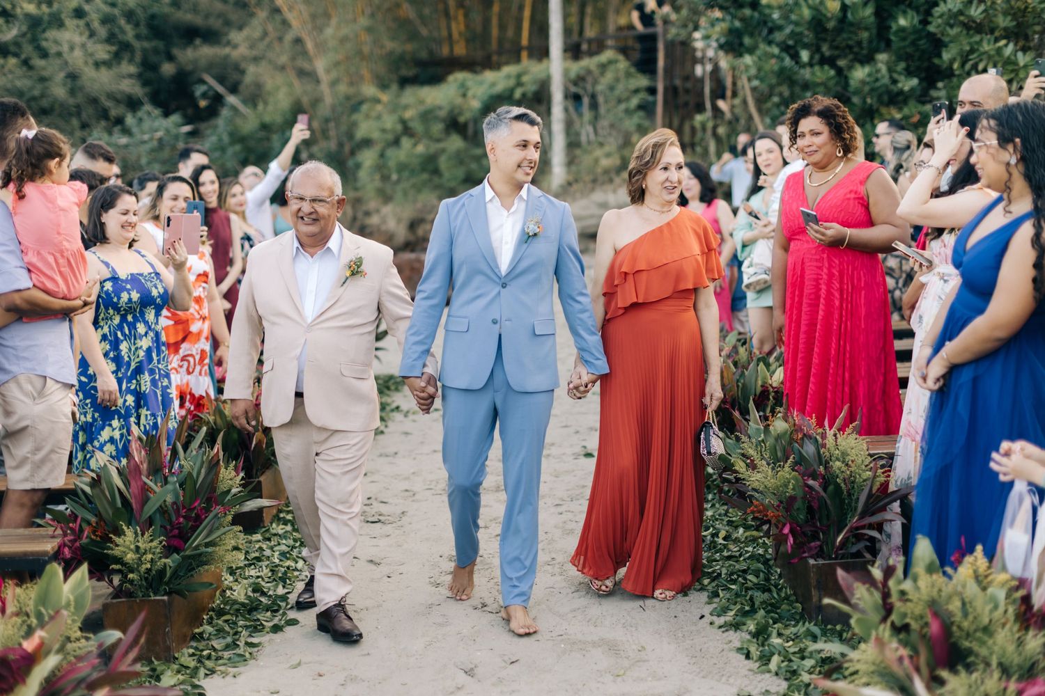 Wedding processional walking down a garden path with guests in colorful dresses watching.