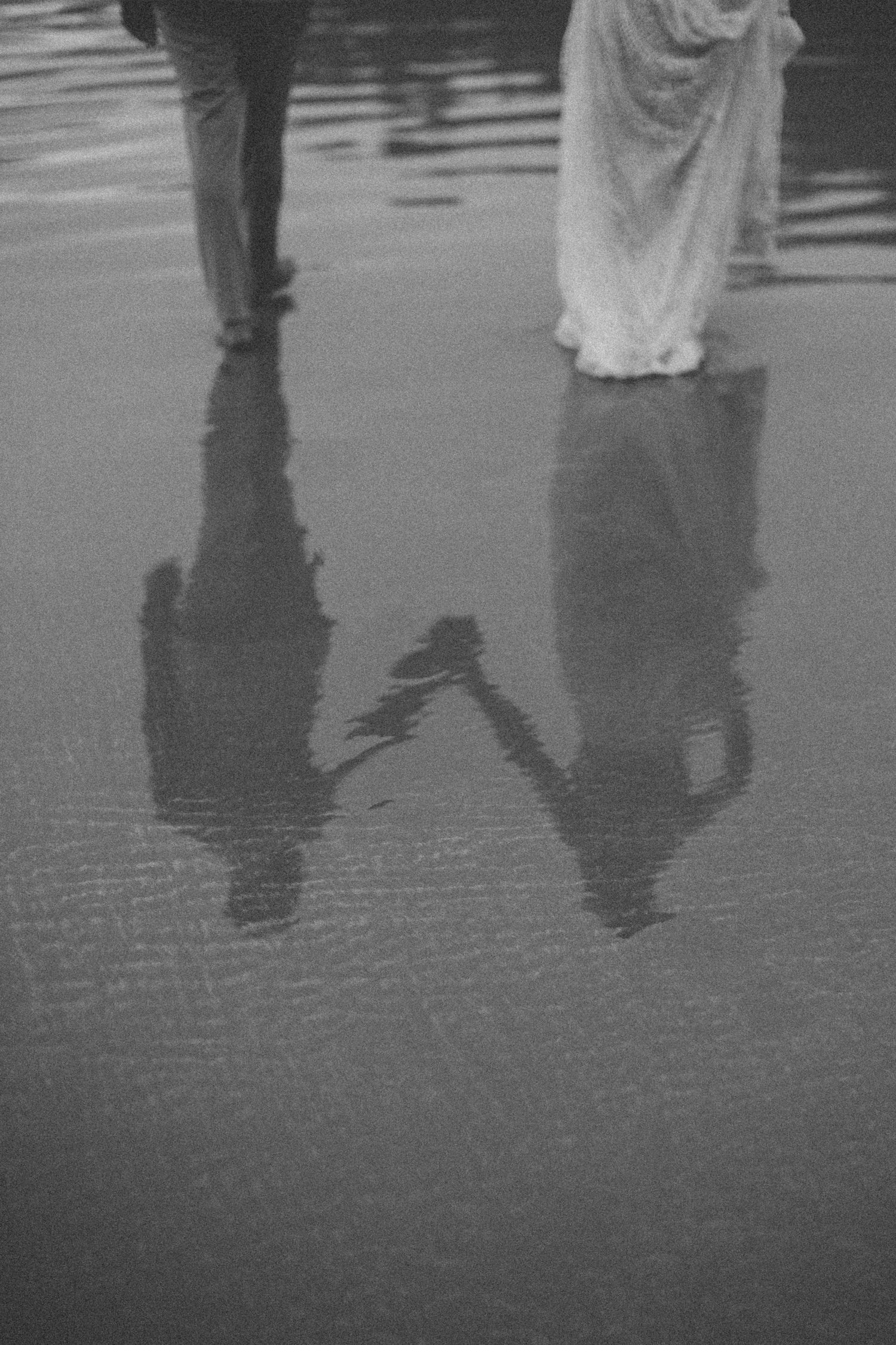 Black and white reflection of couple dancing on wet beach sand.
