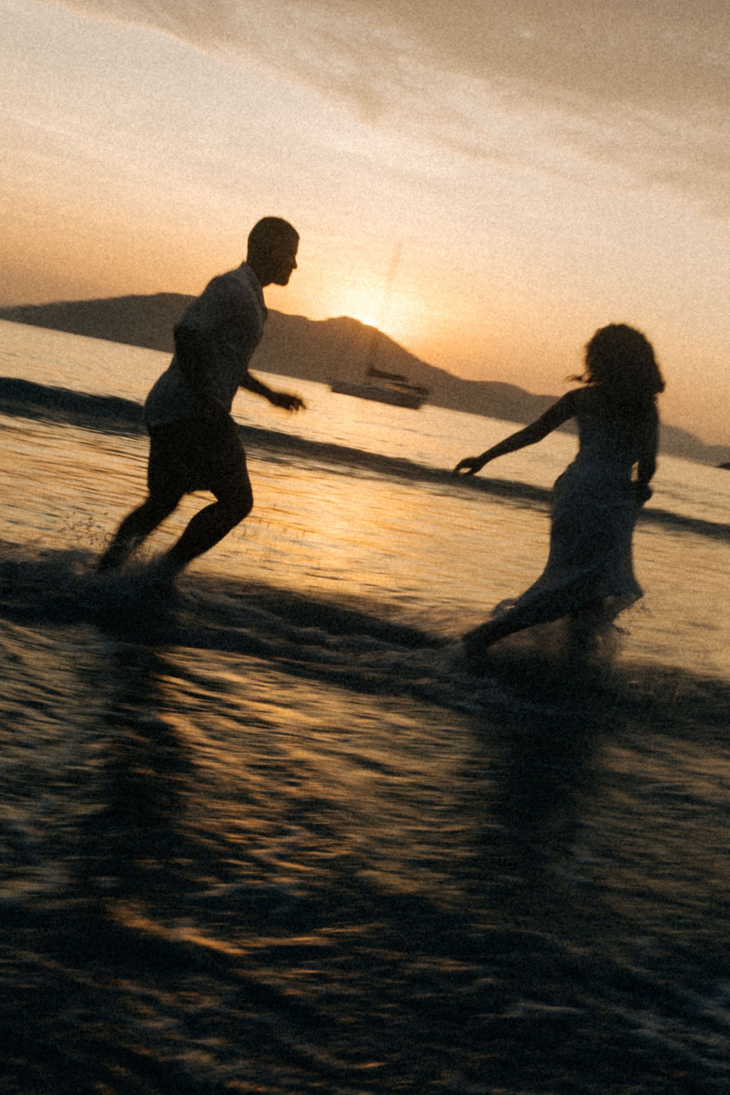 Silhouetted couple playing in ocean water during dramatic sunset.