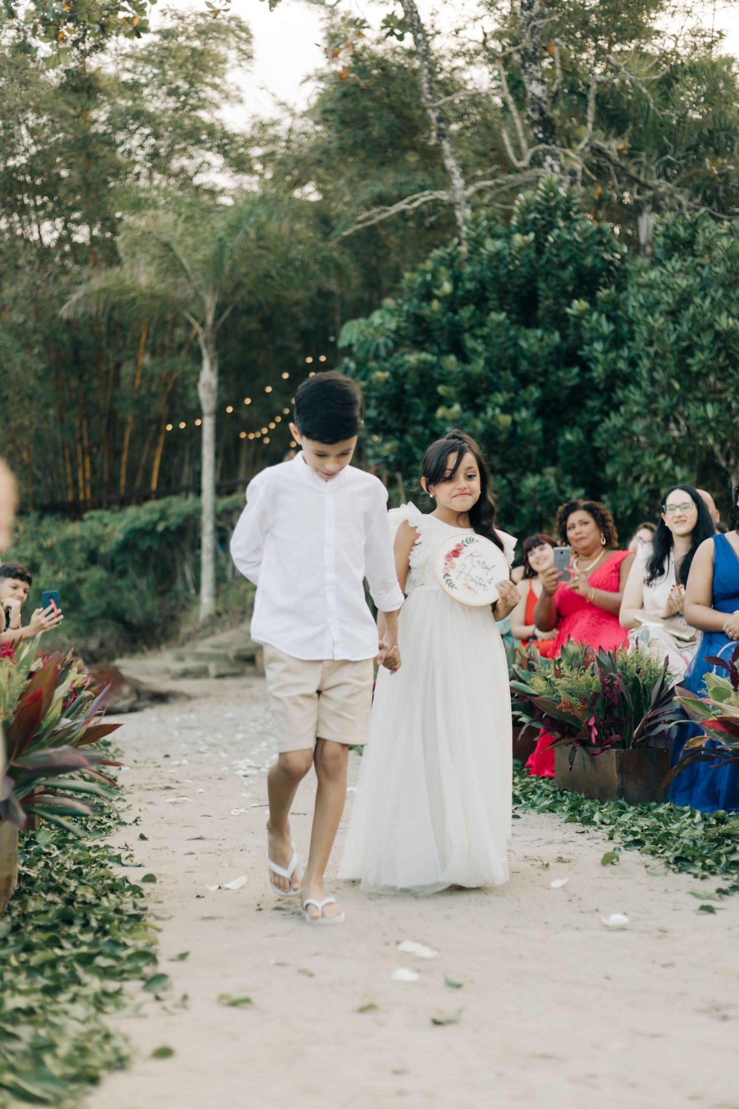 Couple walking down outdoor path with string lights and tropical foliage.