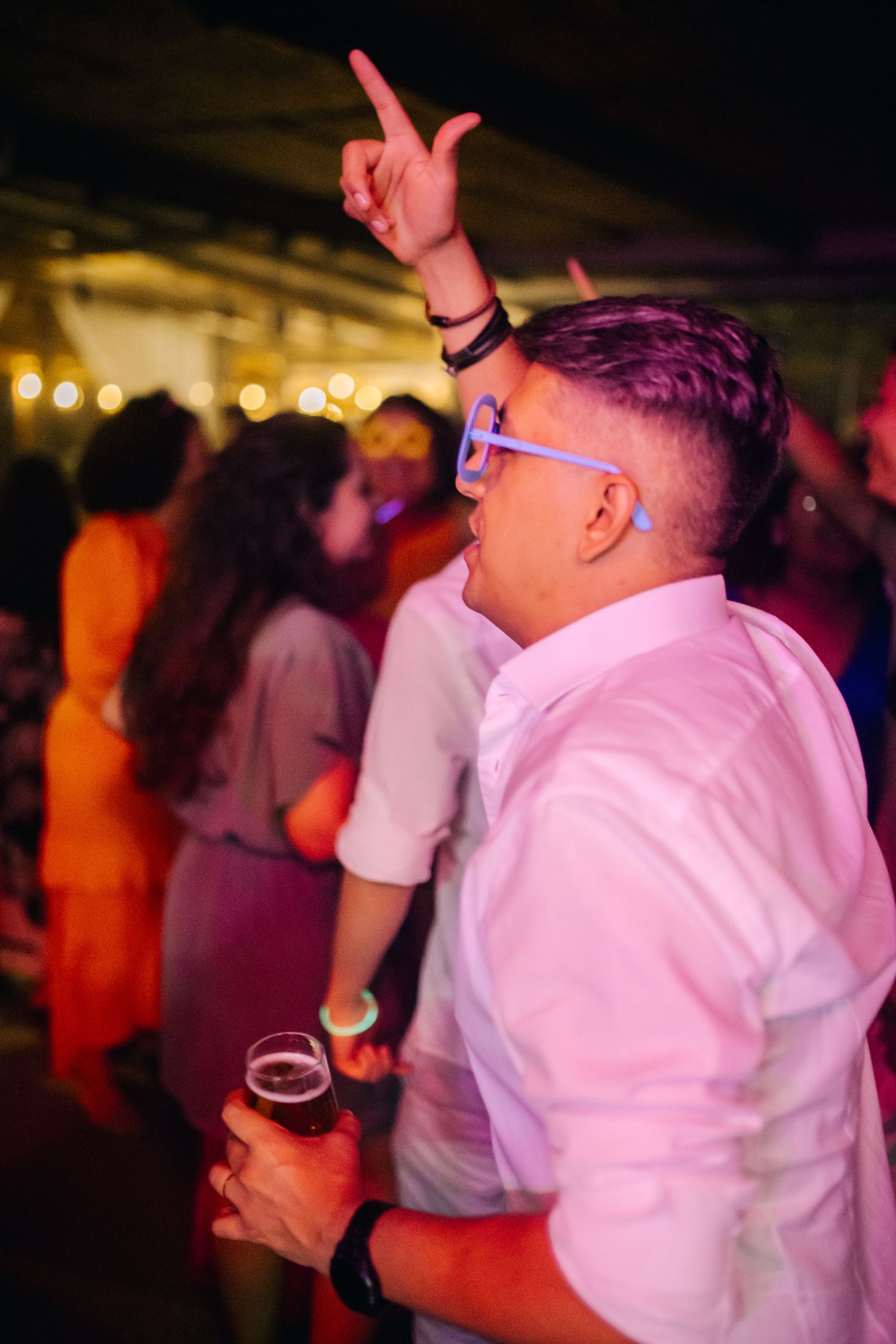 Wedding guests dancing and celebrating under pink mood lighting at a reception.
