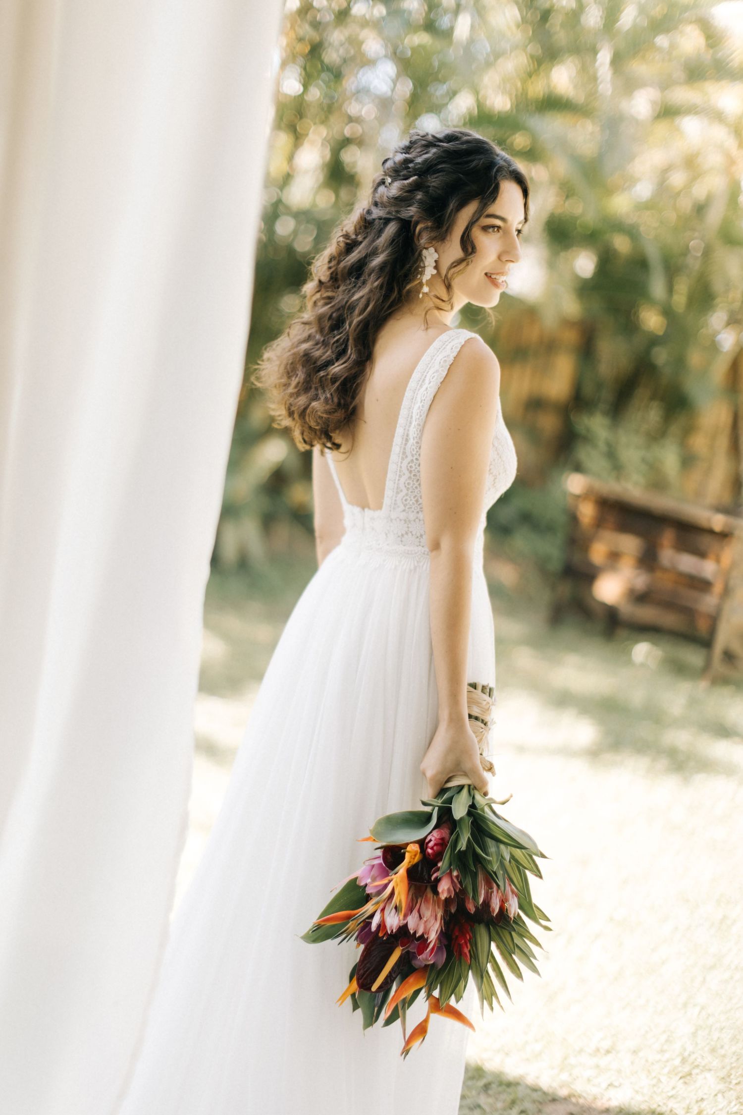 A side view of a bride in a flowing white dress holding tropical flowers.