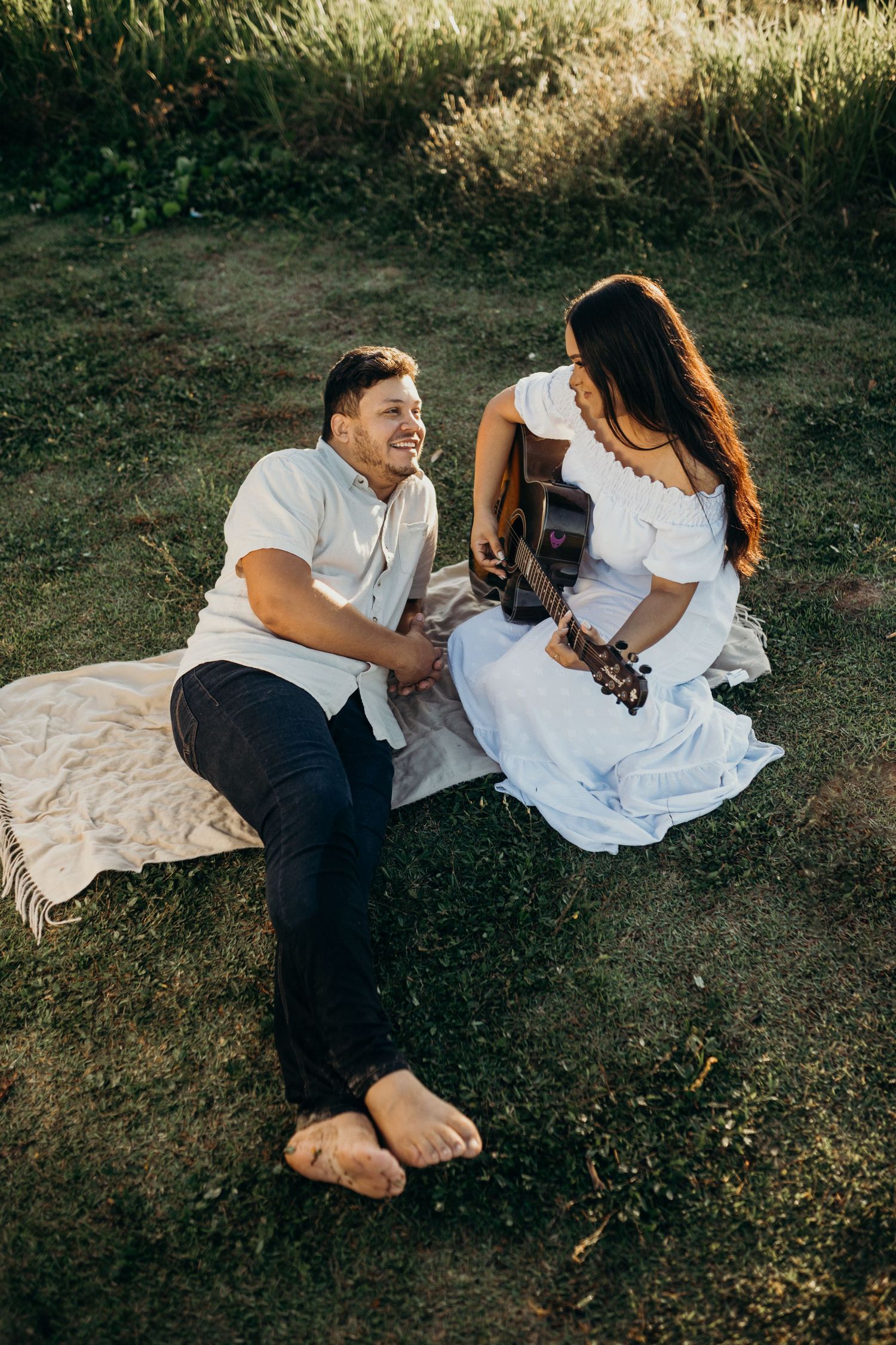 Couple sharing intimate moment while sitting on blanket in grassy field at sunset.