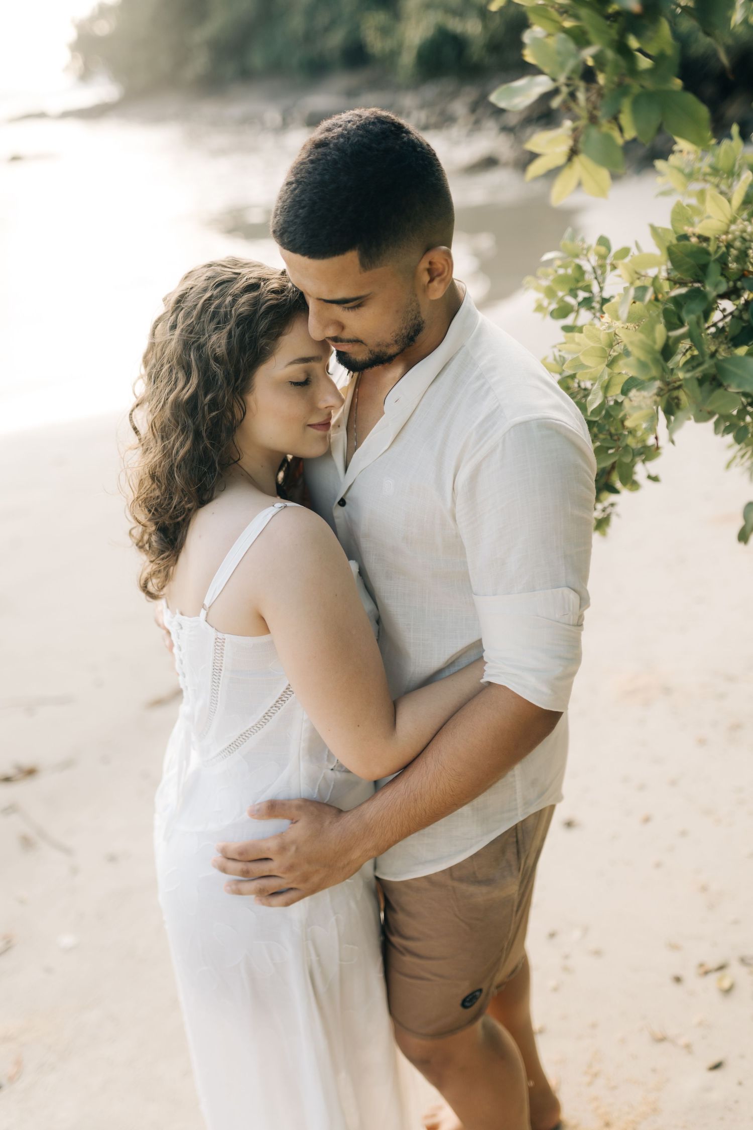 Tender moment between couple in casual beach attire during sunset photoshoot.
