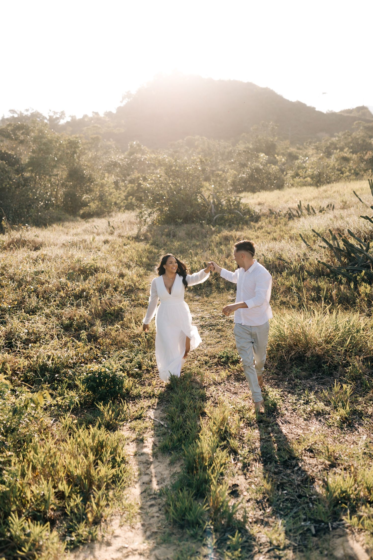 A couple in white clothing dances together on a sunlit mountain trail.