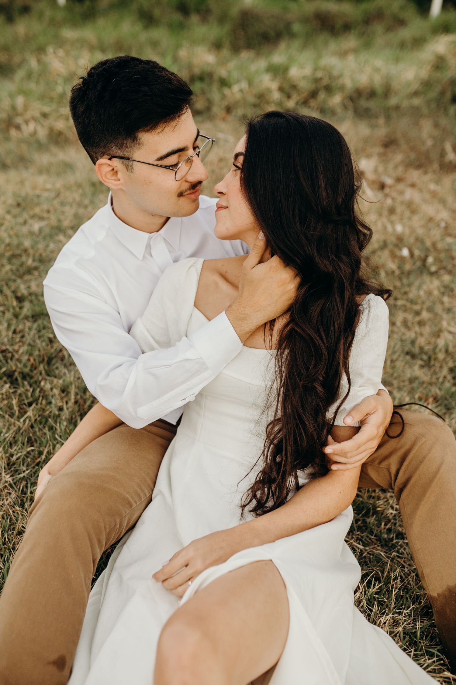 A couple sharing an intimate moment while sitting in a grassy field.