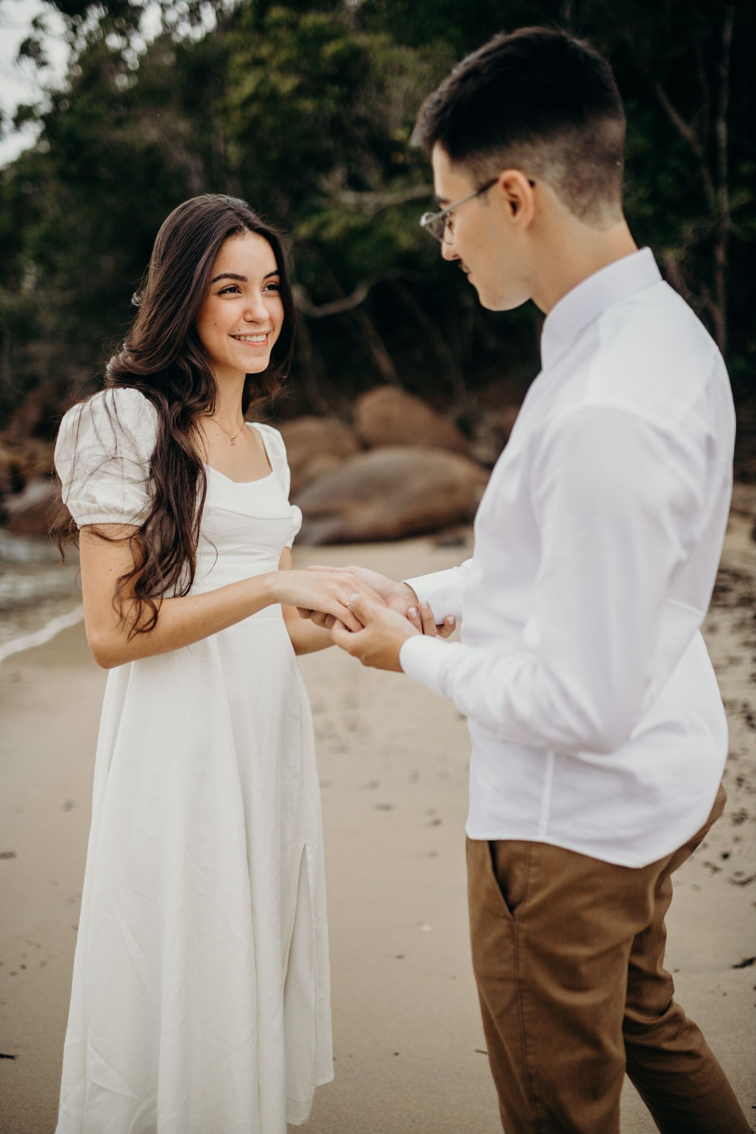 A couple in white and brown outfits share tender moments during their beach photoshoot.