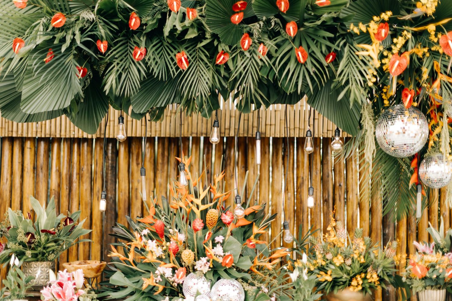 Close-up of tropical floral arrangement with orange blooms and hanging disco balls on bamboo background.