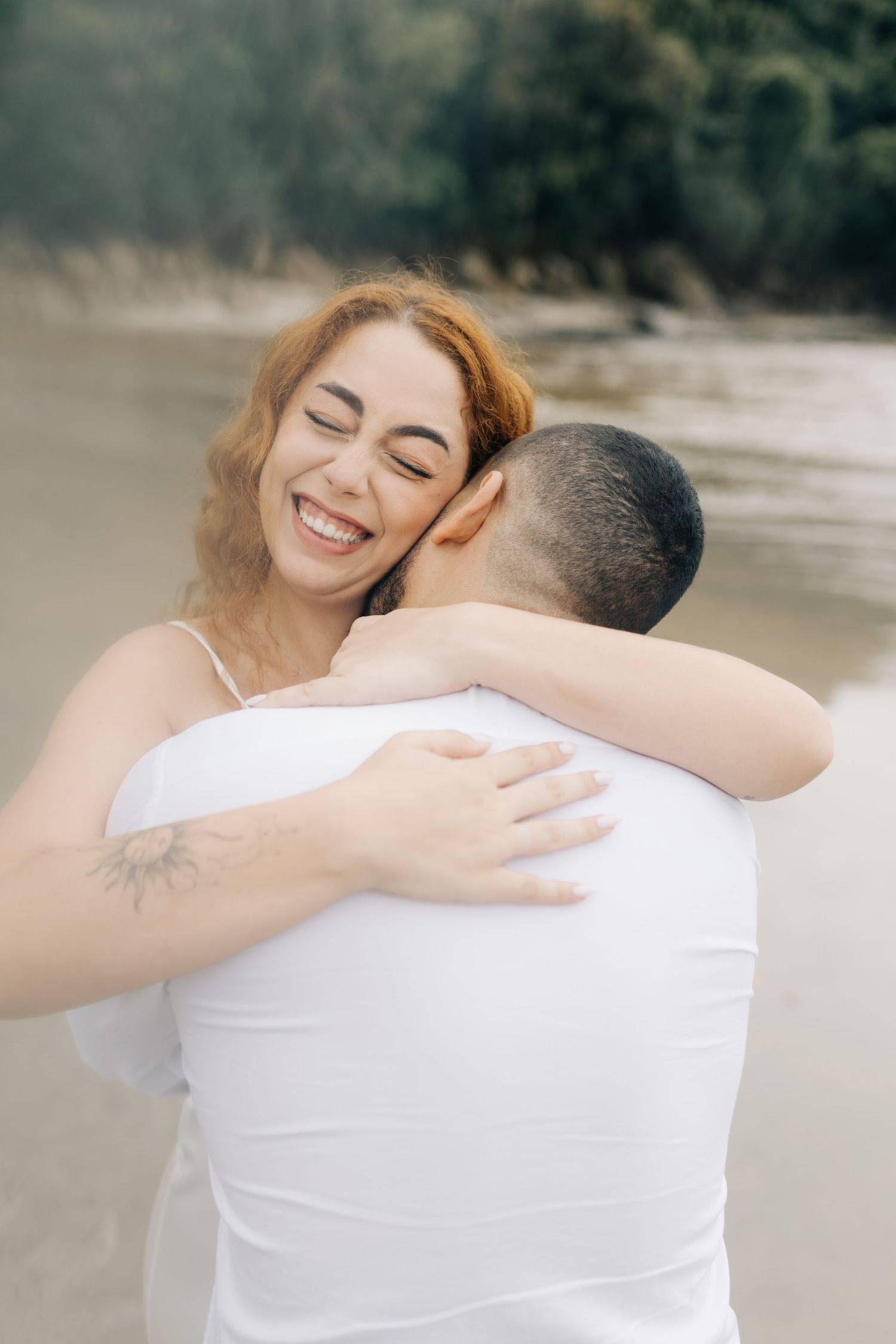 An intimate beach photo showing a happy couple sharing a warm embrace against a misty coastal backdrop.