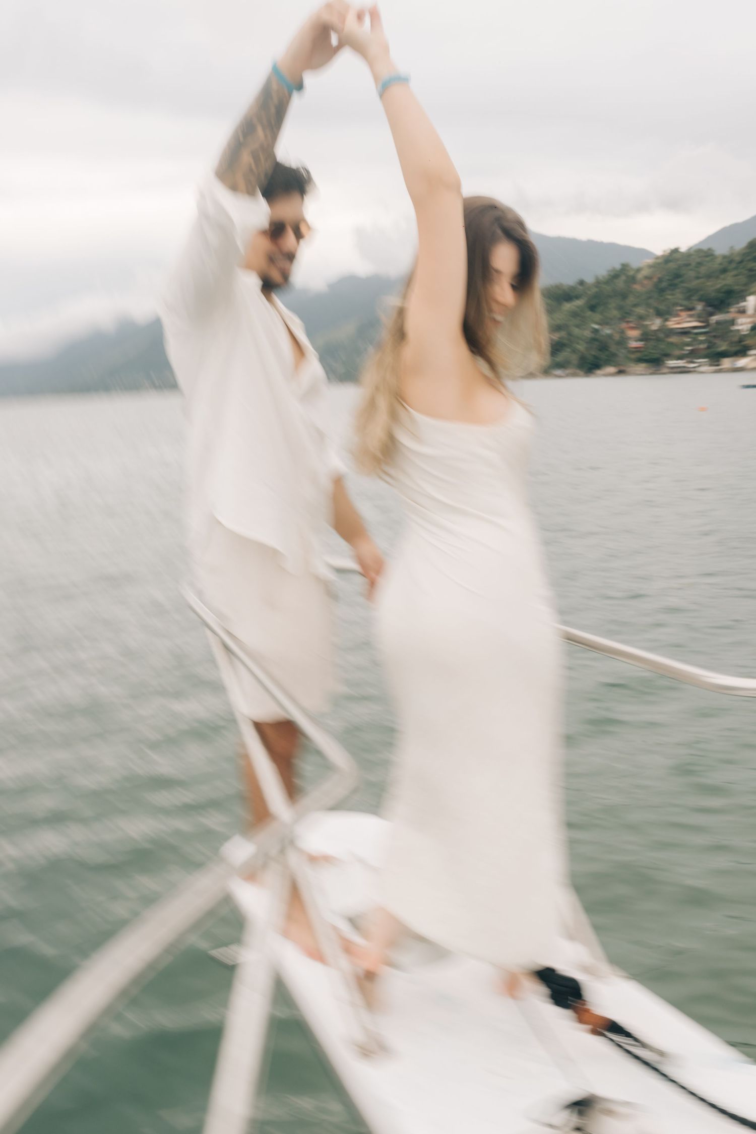 Couple in white attire dancing and twirling on a boat with mountains in the distance.