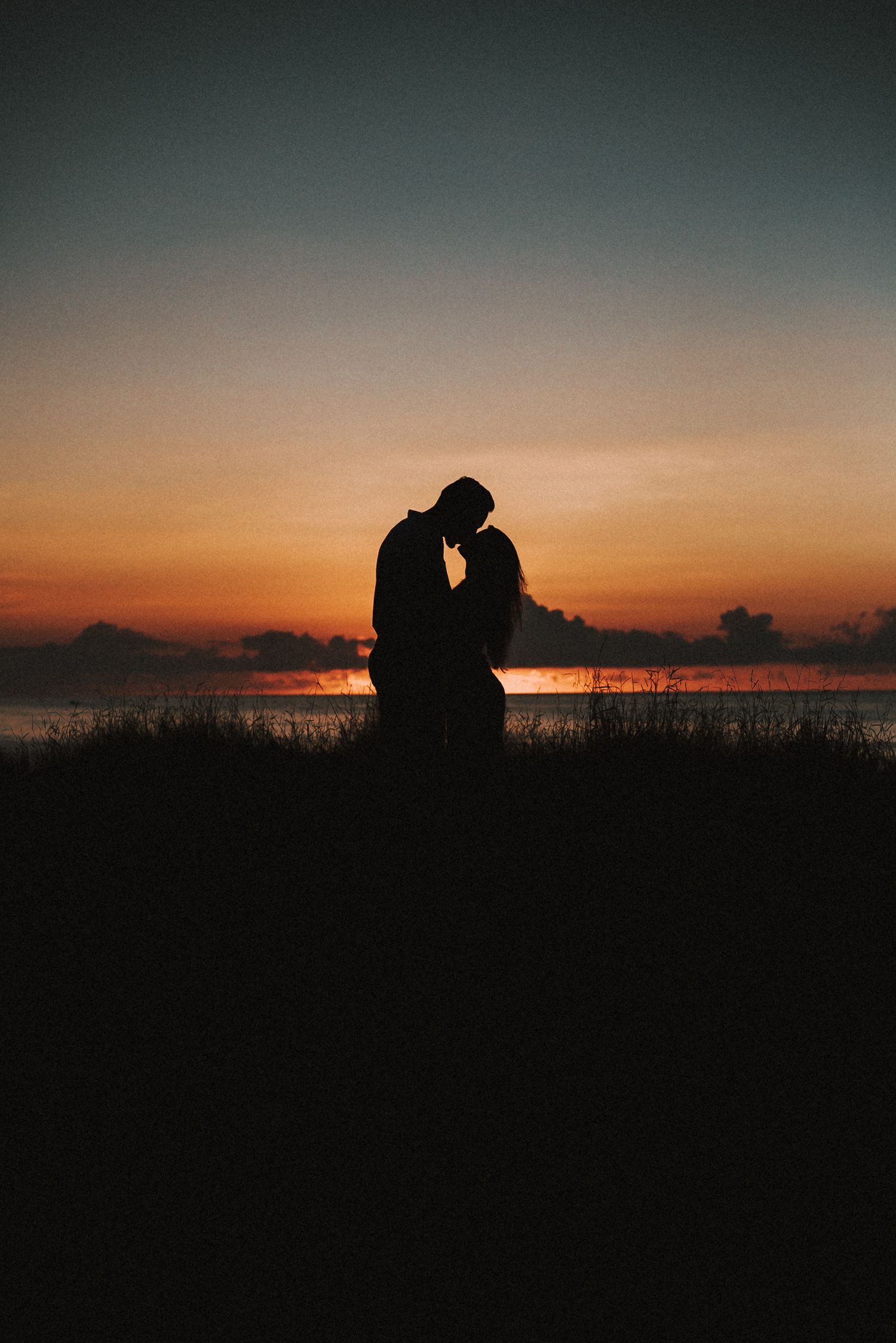 Dark silhouettes of two people embracing during golden hour at a scenic coastal location.