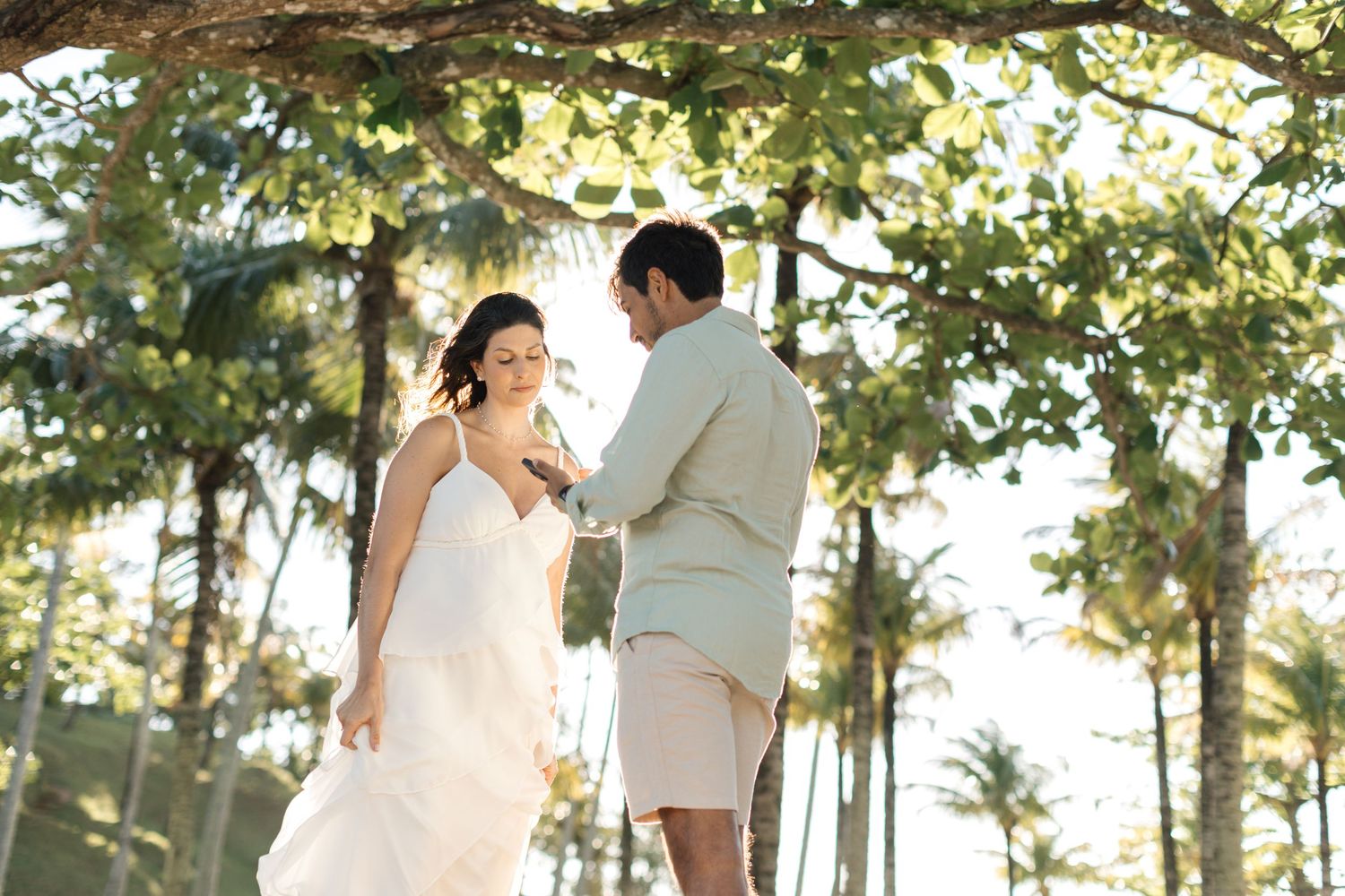 A couple shares a romantic moment under palm trees during their beach wedding ceremony.