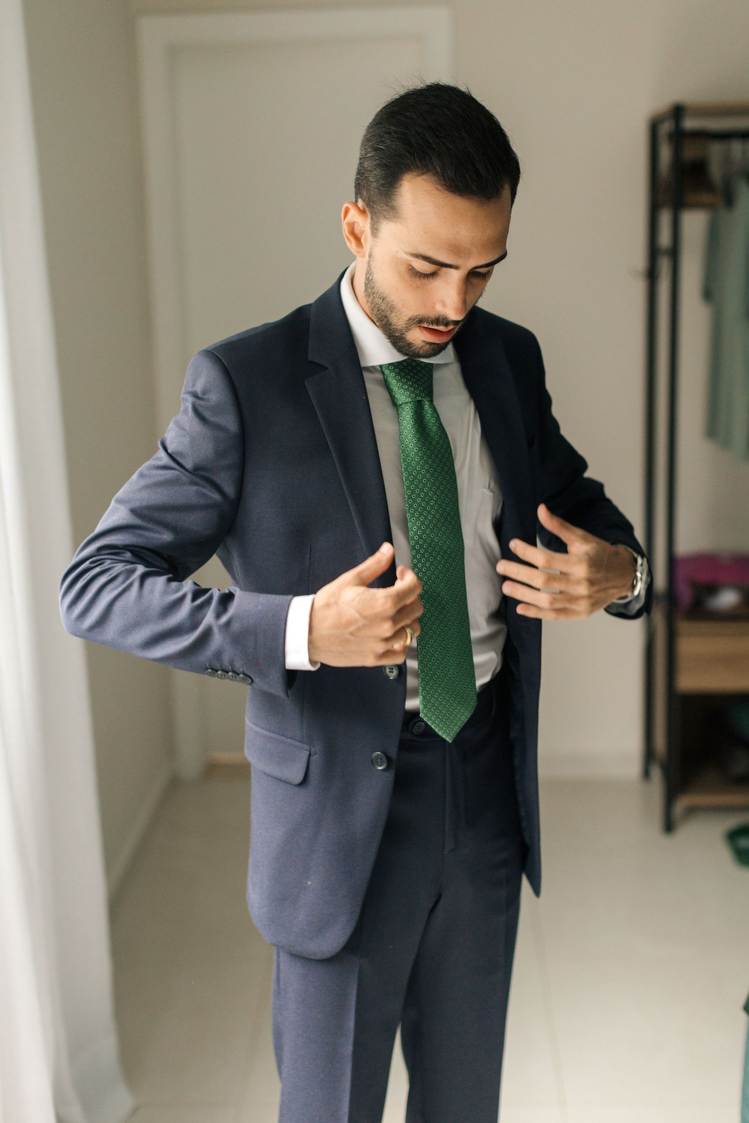 Professional in a navy suit and emerald green tie adjusts his jacket while getting dressed.
