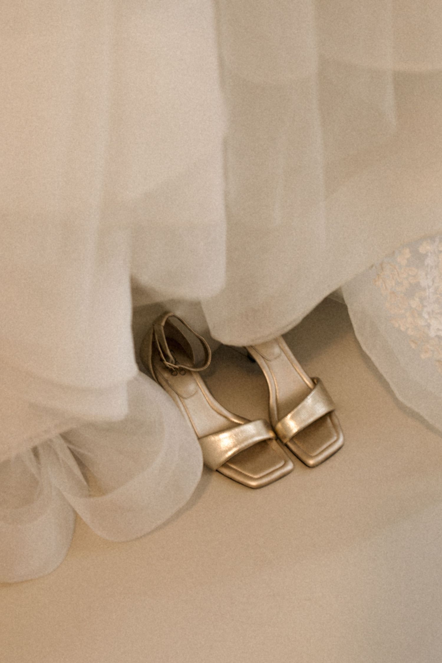 Gold wedding shoes peek out beneath layers of flowing white tulle fabric in an elegant bridal detail shot.