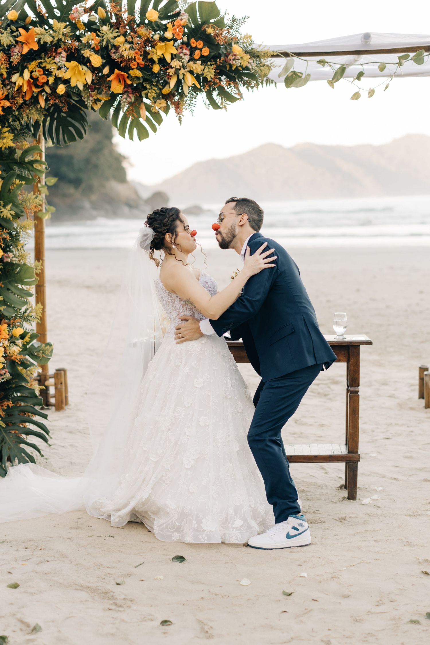 Romantic embrace under floral arch during sunset beach wedding ceremony.