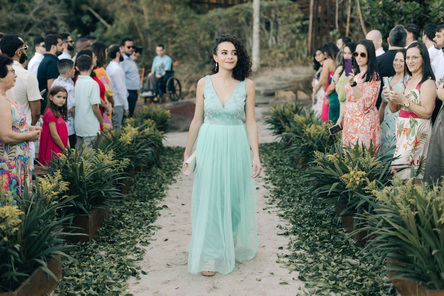 A bridesmaid in a mint green dress walks down an outdoor garden aisle.