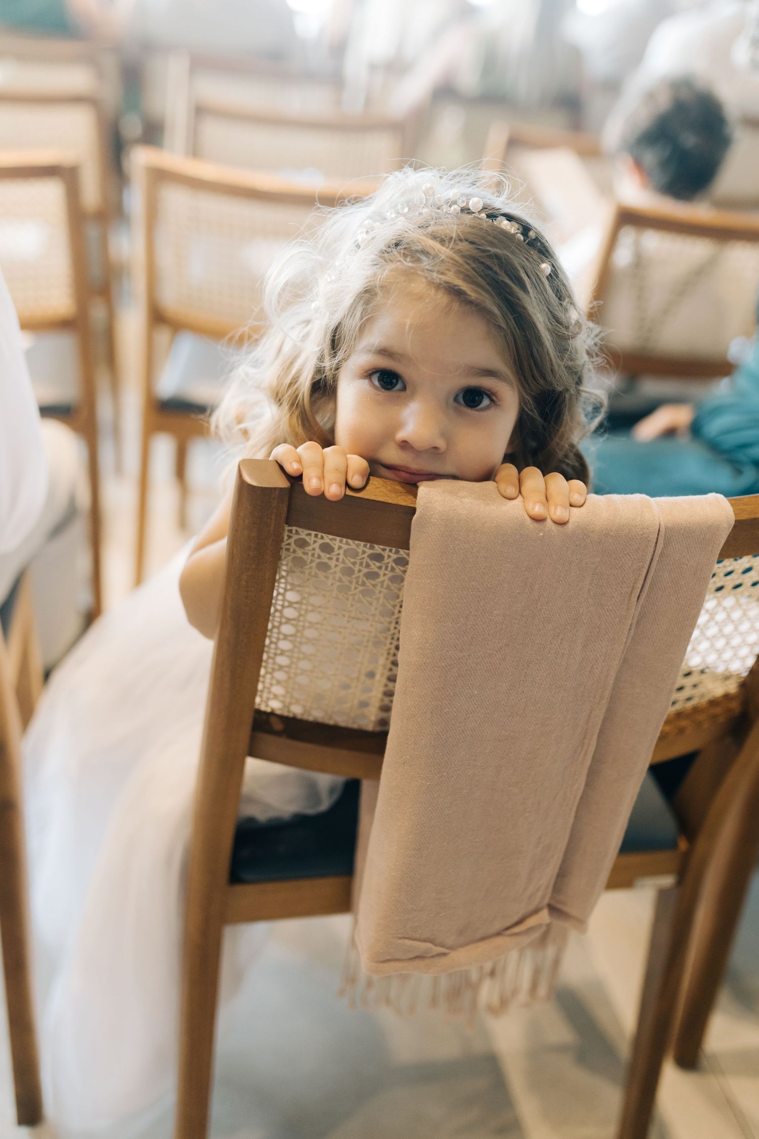 Young event guest playfully peeks over dining chair at formal gathering.